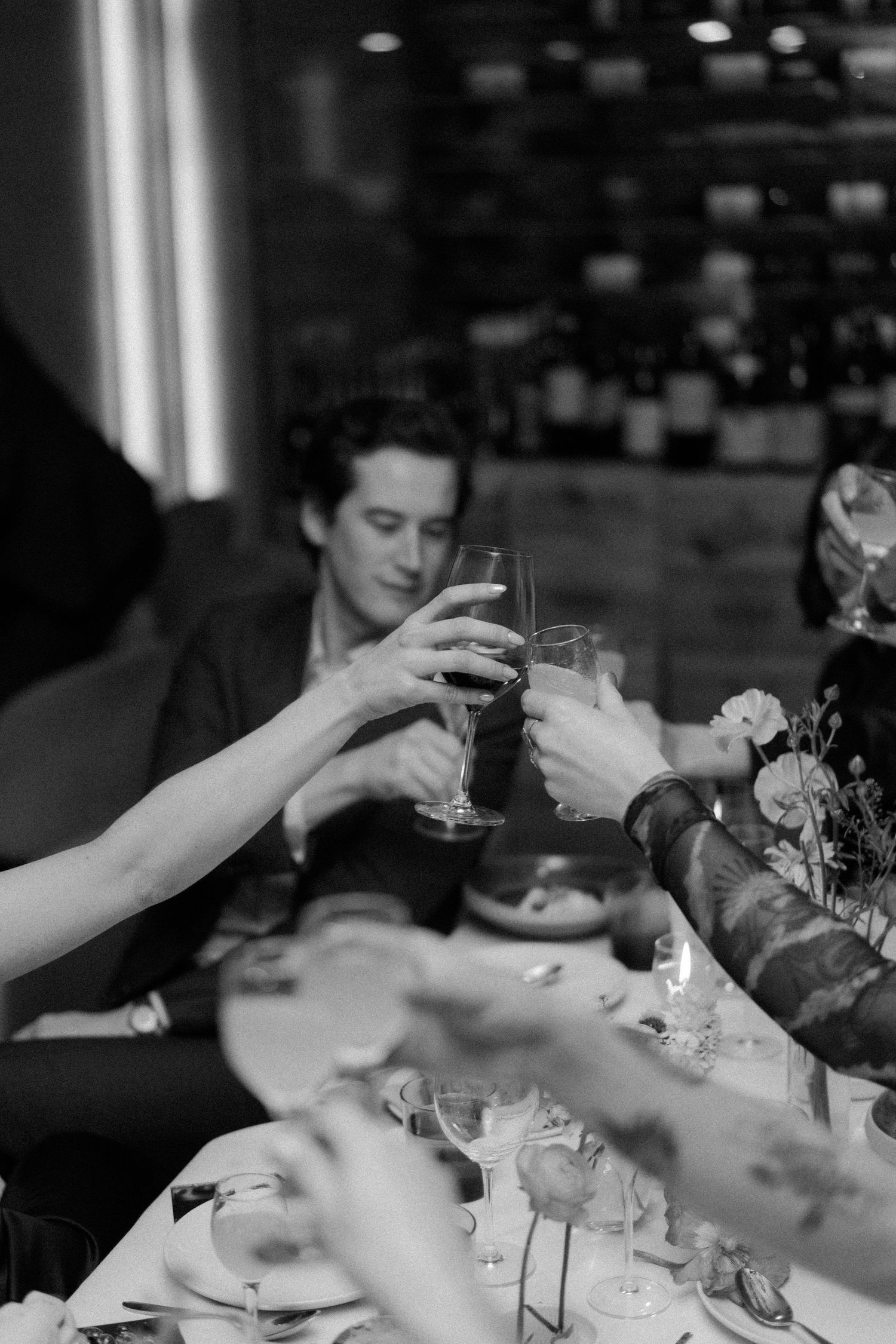 Guests clink wine glasses in a toast at an elegant wedding reception dinner in black and white photo.