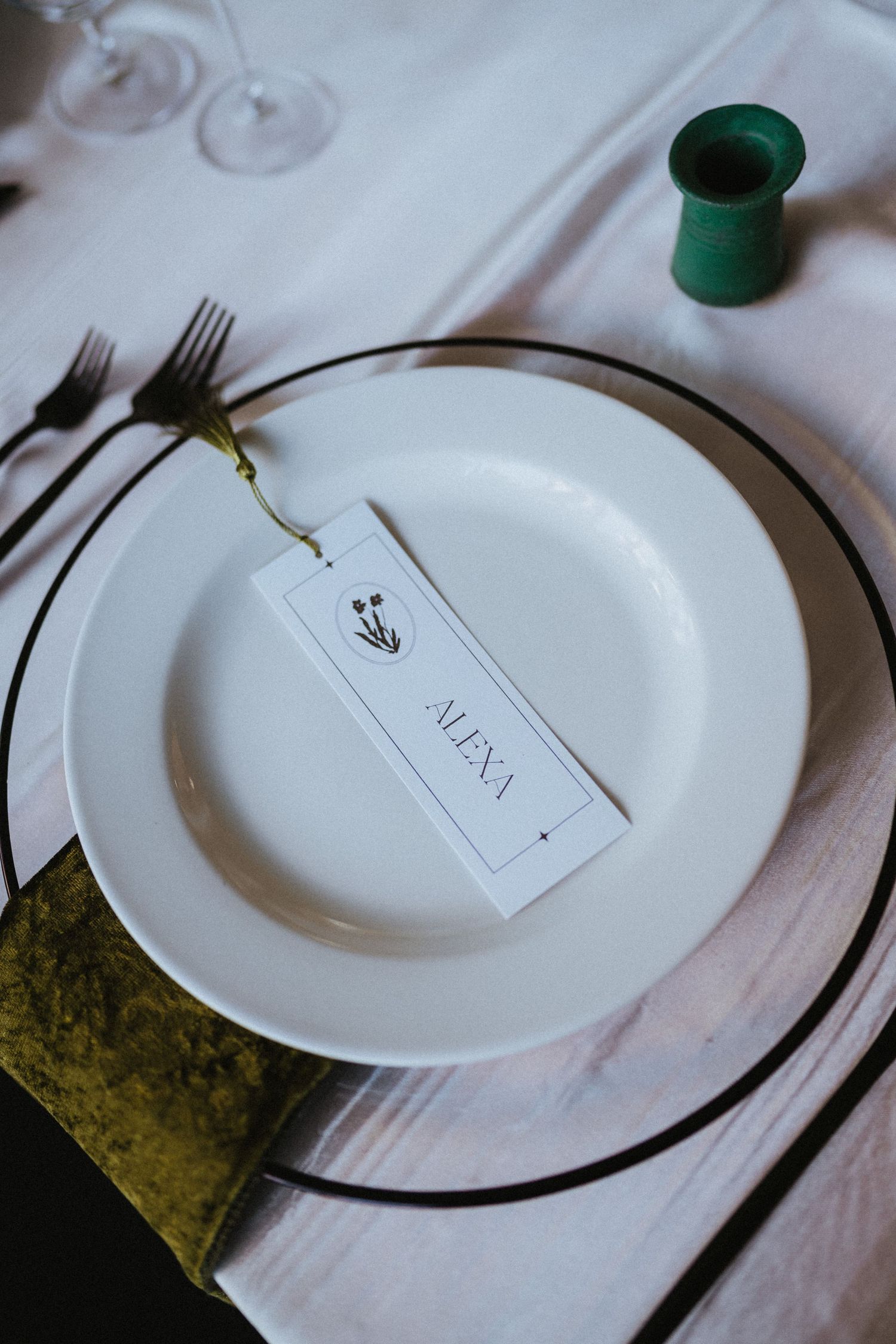 Elegant place setting with white plate, name card reading Alexa, green velvet napkin, and small green candleholder.