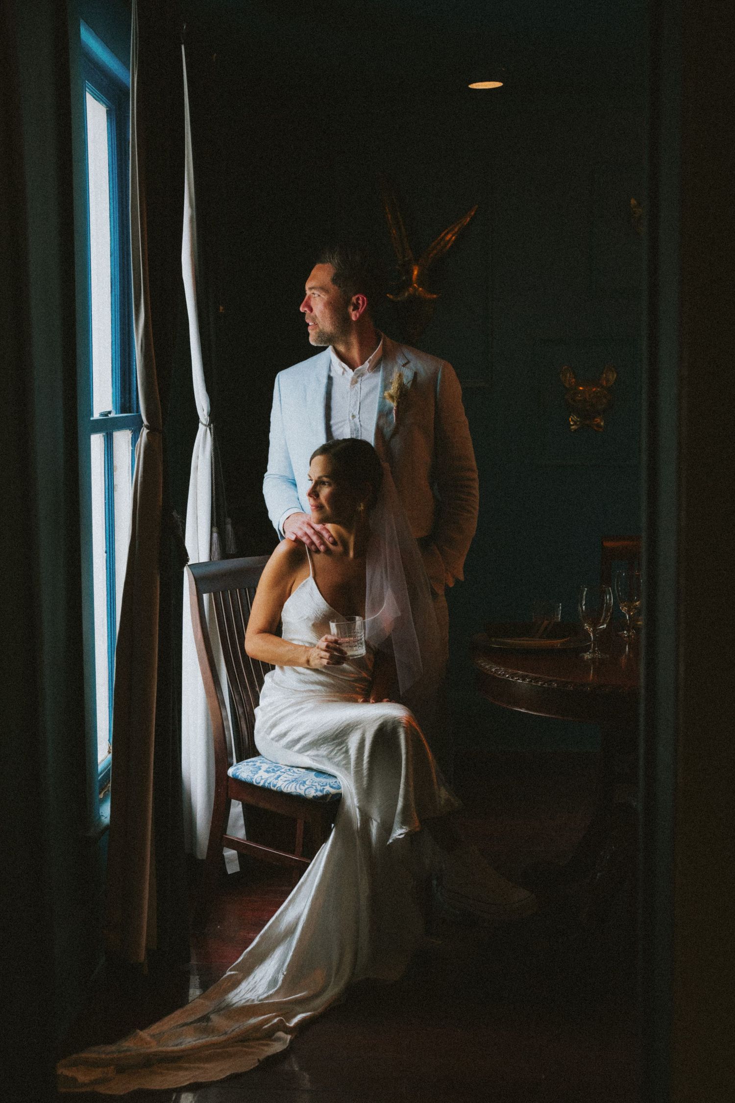A couple shares an intimate dance in a dimly lit room with large windows casting dramatic shadows.