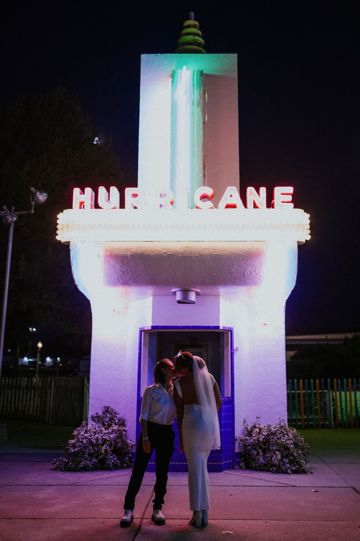 A lighthouse illuminated with purple and white lights at night creates a romantic atmosphere for a couple.