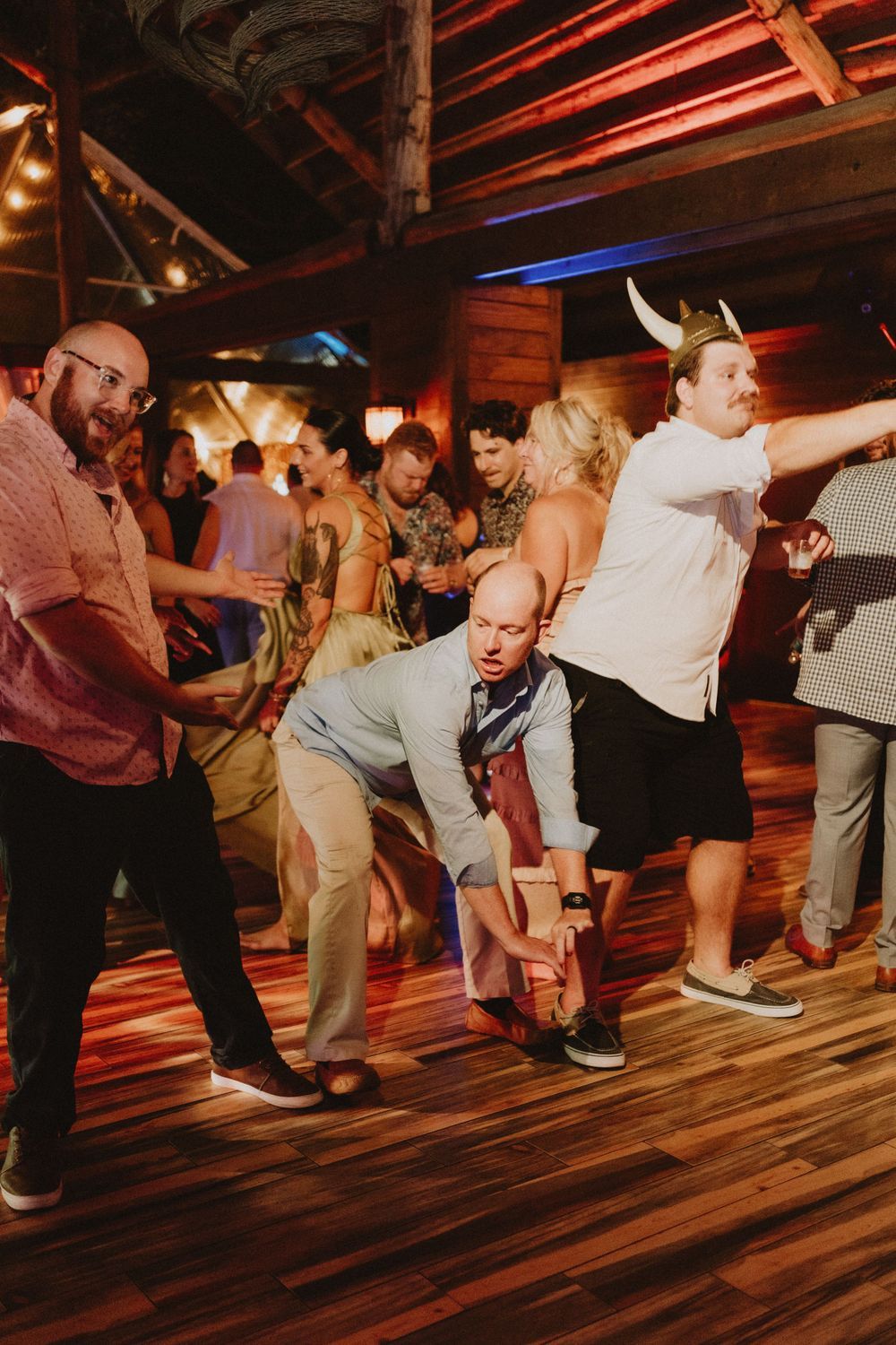 Group of wedding guests performing a choreographed dance on wooden floor.