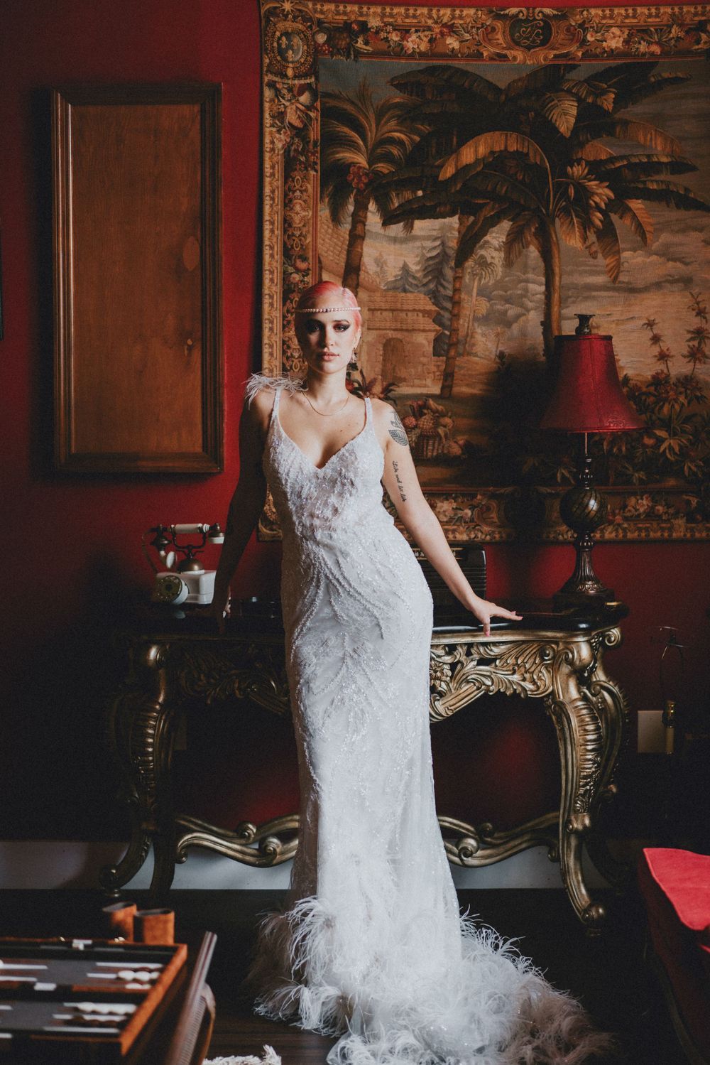 Ethereal white wedding gown with feather details against red wall and vintage furniture.