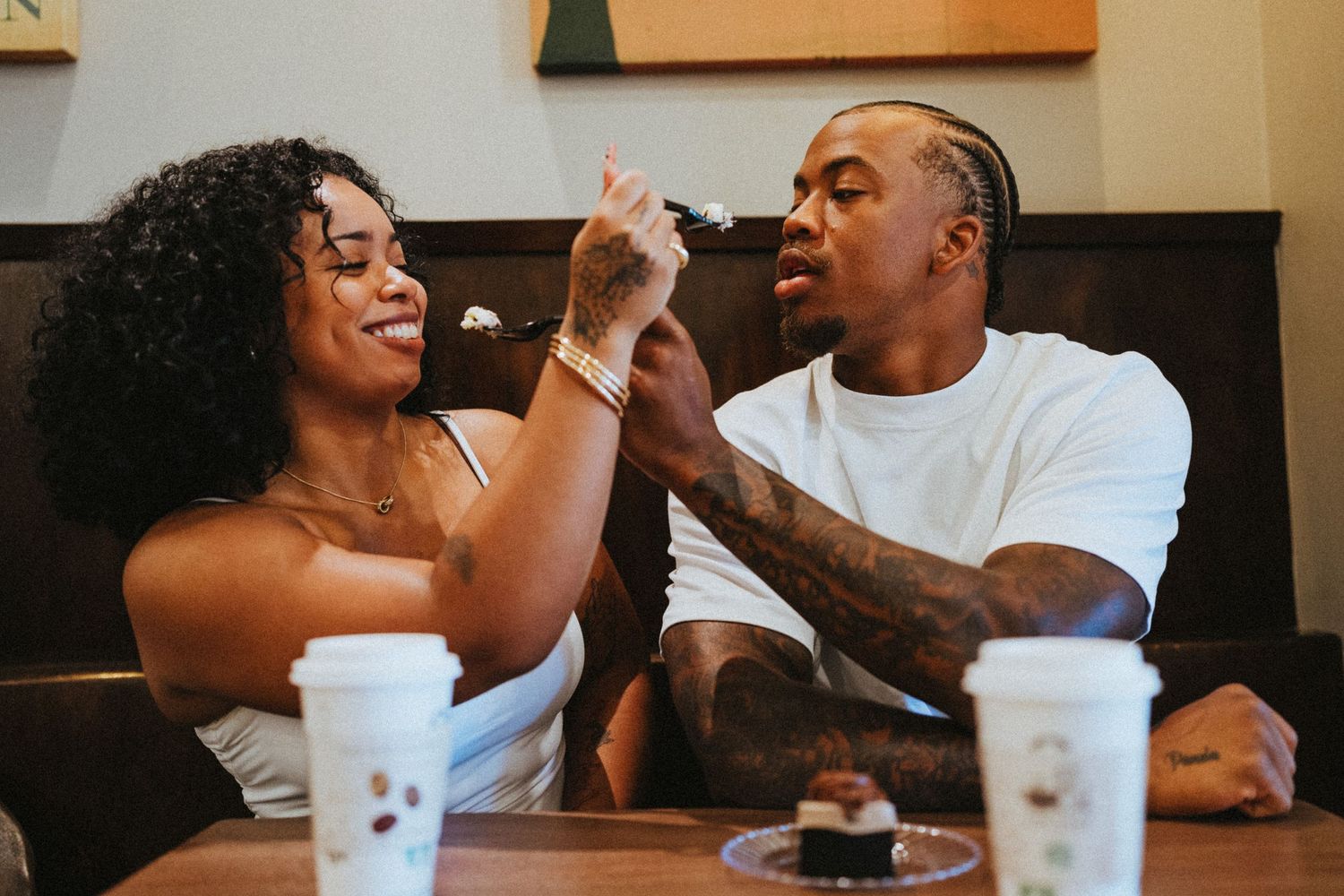 A couple sharing dessert and laughing together at a cozy cafe, with coffee cups on the table.