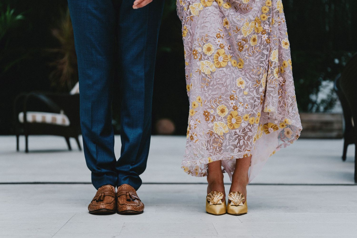 Couple standing together showing brown tassel loafers and gold floral heels with blue suit and floral dress.