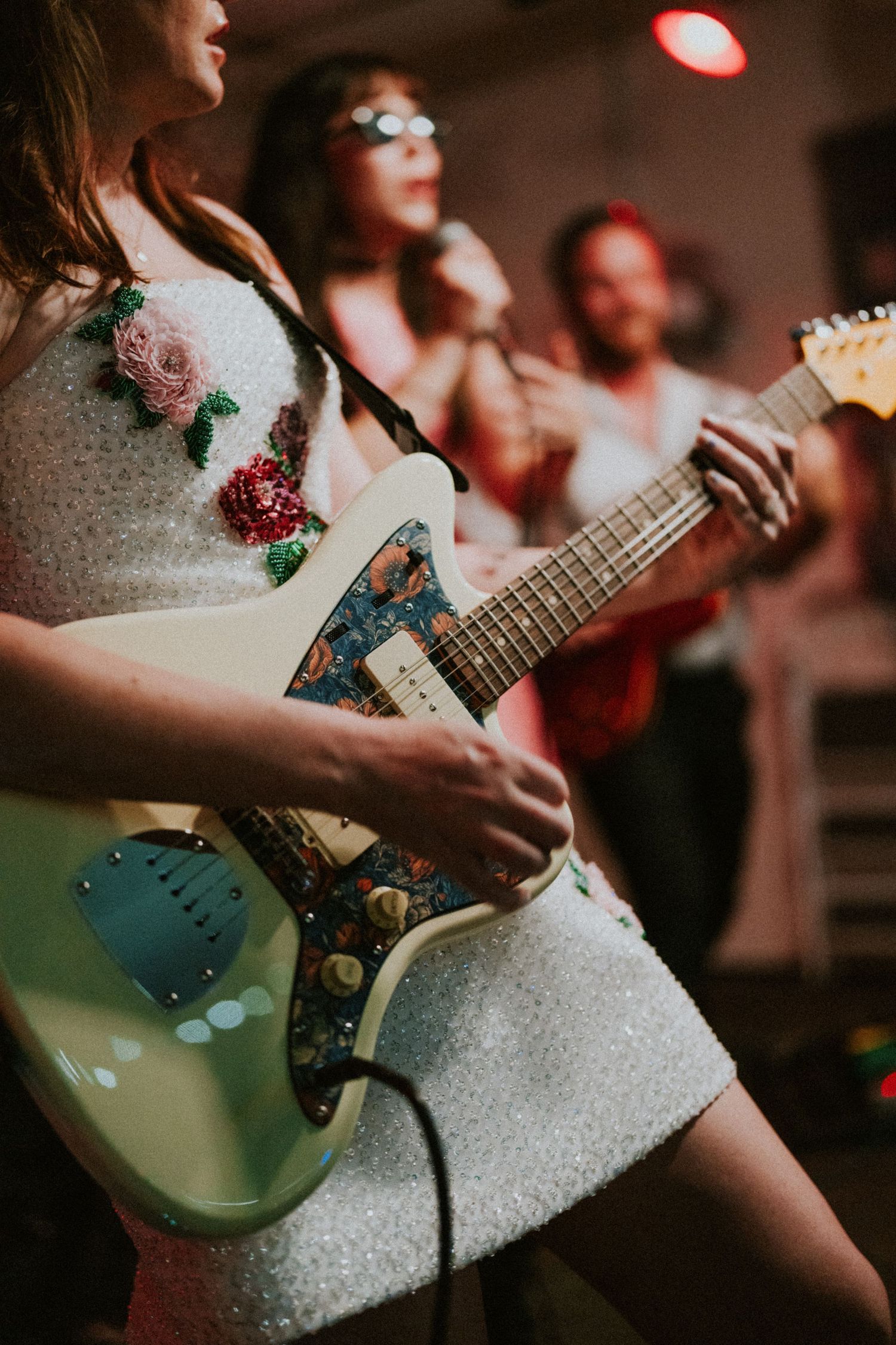 Bride playing a mint green electric guitar in a floral embellished white dress at wedding reception.