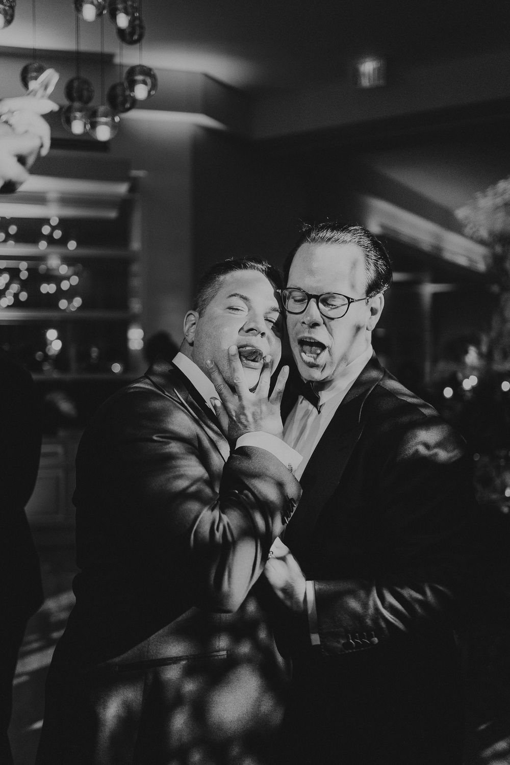 Two people sharing joyful laughter at a wedding reception in black and white.