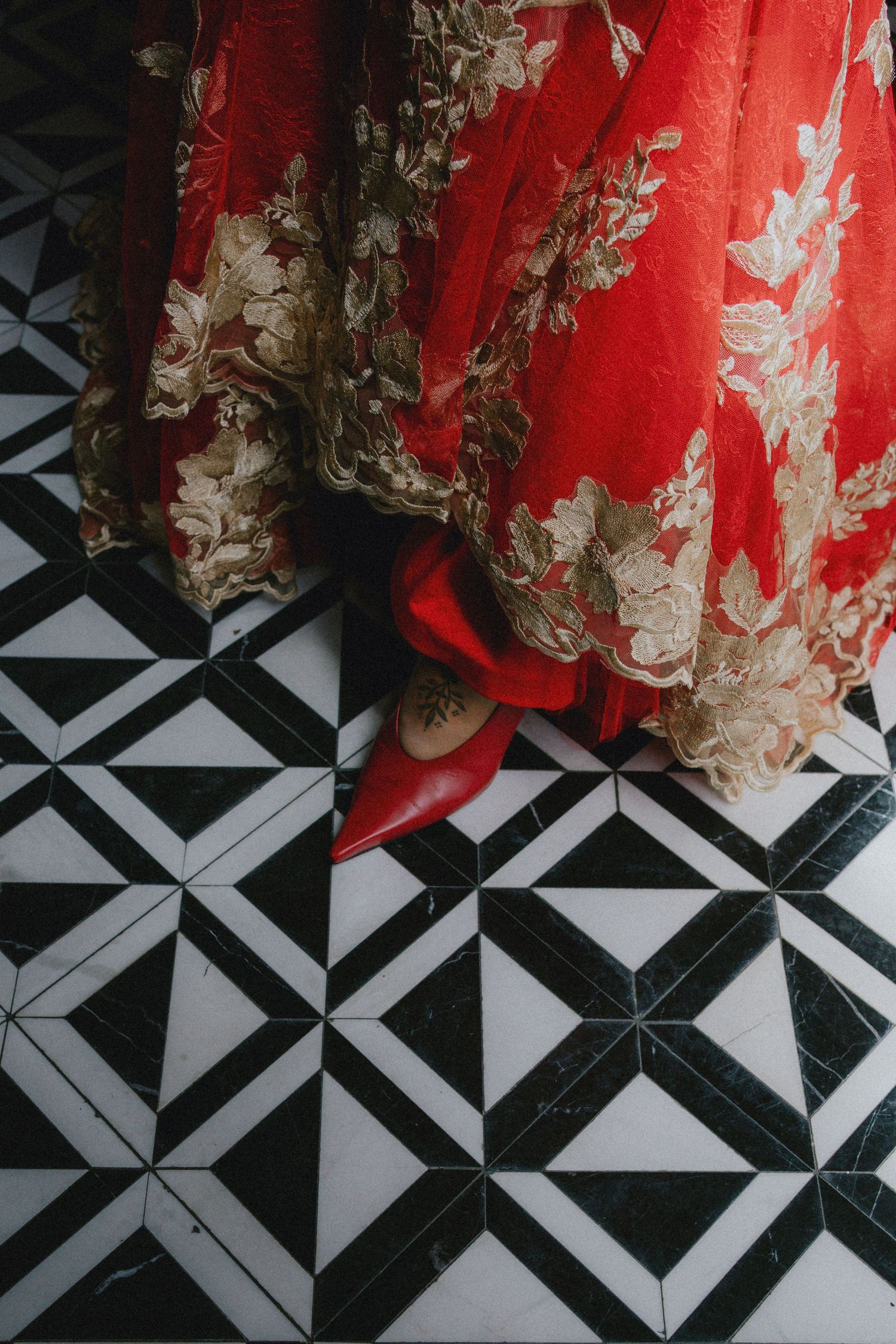 Red and gold embroidered lehenga with matching red heels on black and white geometric marble tile floor.