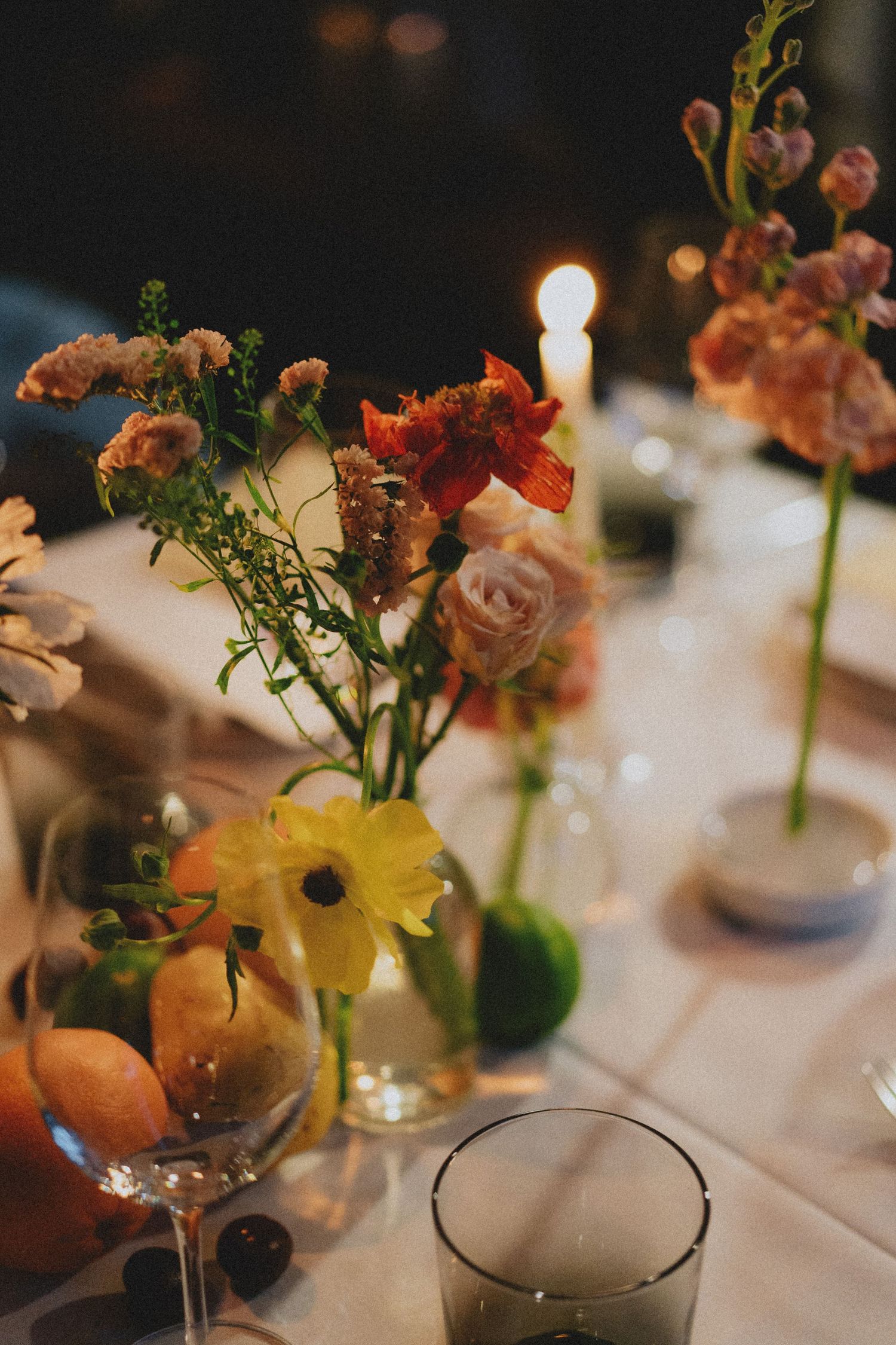 Colorful wildflower centerpieces with candles on a white tablecloth at an elegant evening dinner party.