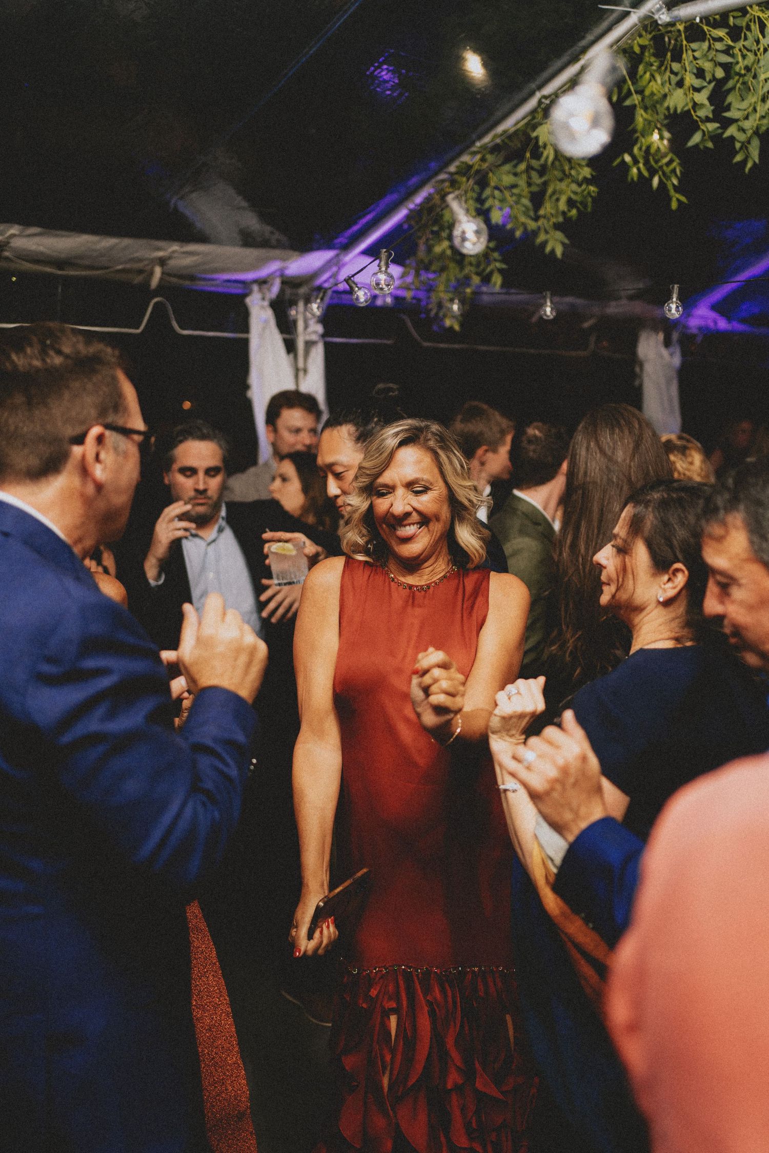 Woman in red dress smiles joyfully while dancing at an outdoor tented wedding reception at night.