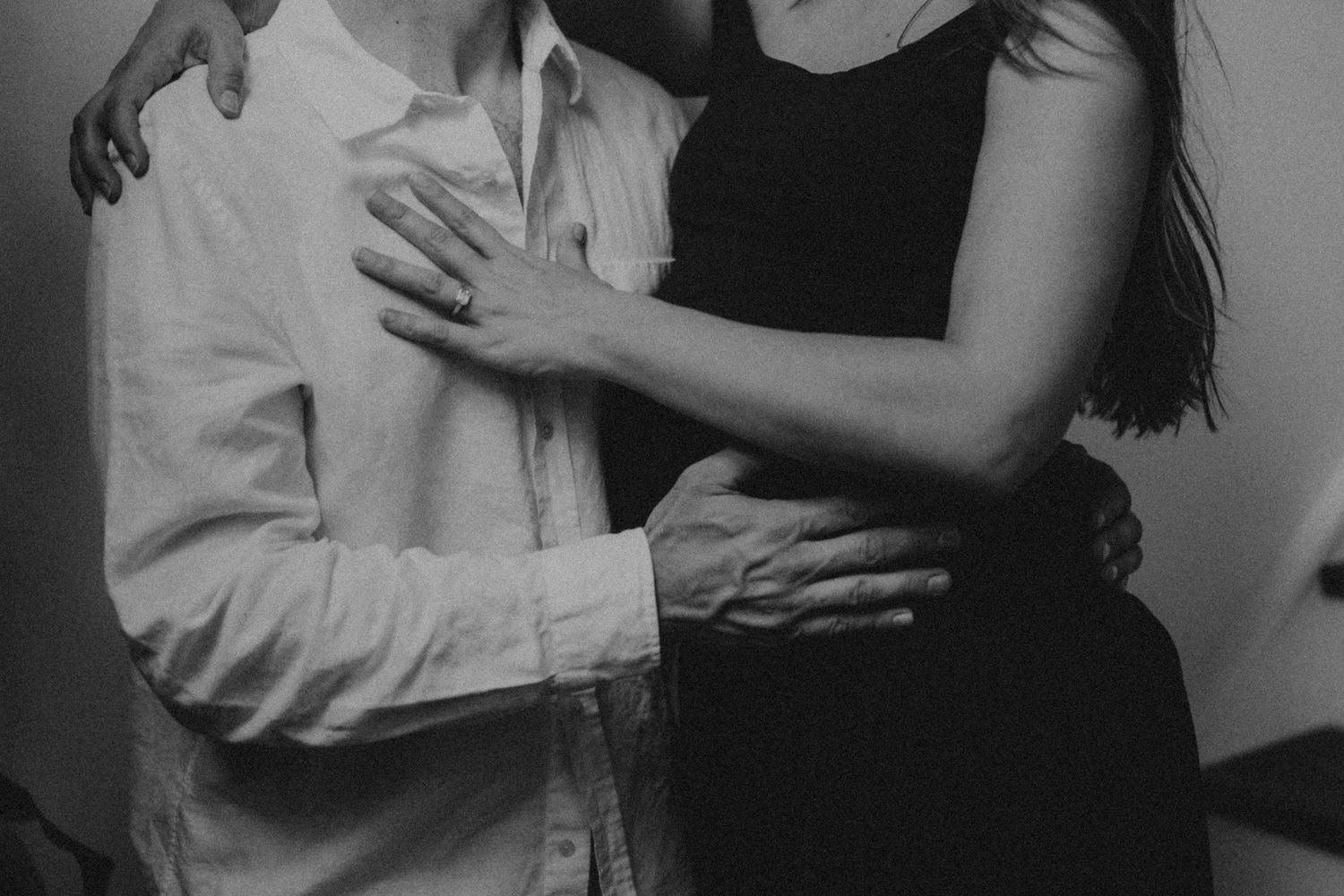 Black and white photo of a couple embracing intimately, woman in black dress with arms around man in white shirt.