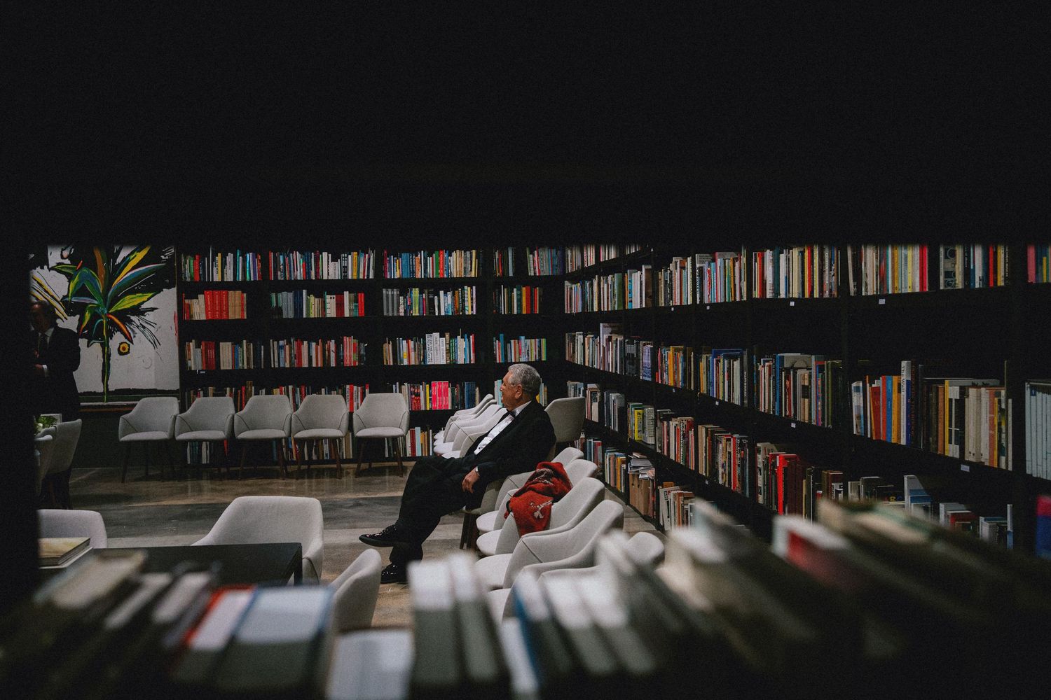 Elderly man relaxing in a cozy library surrounded by floor-to-ceiling bookshelves filled with colorful books.