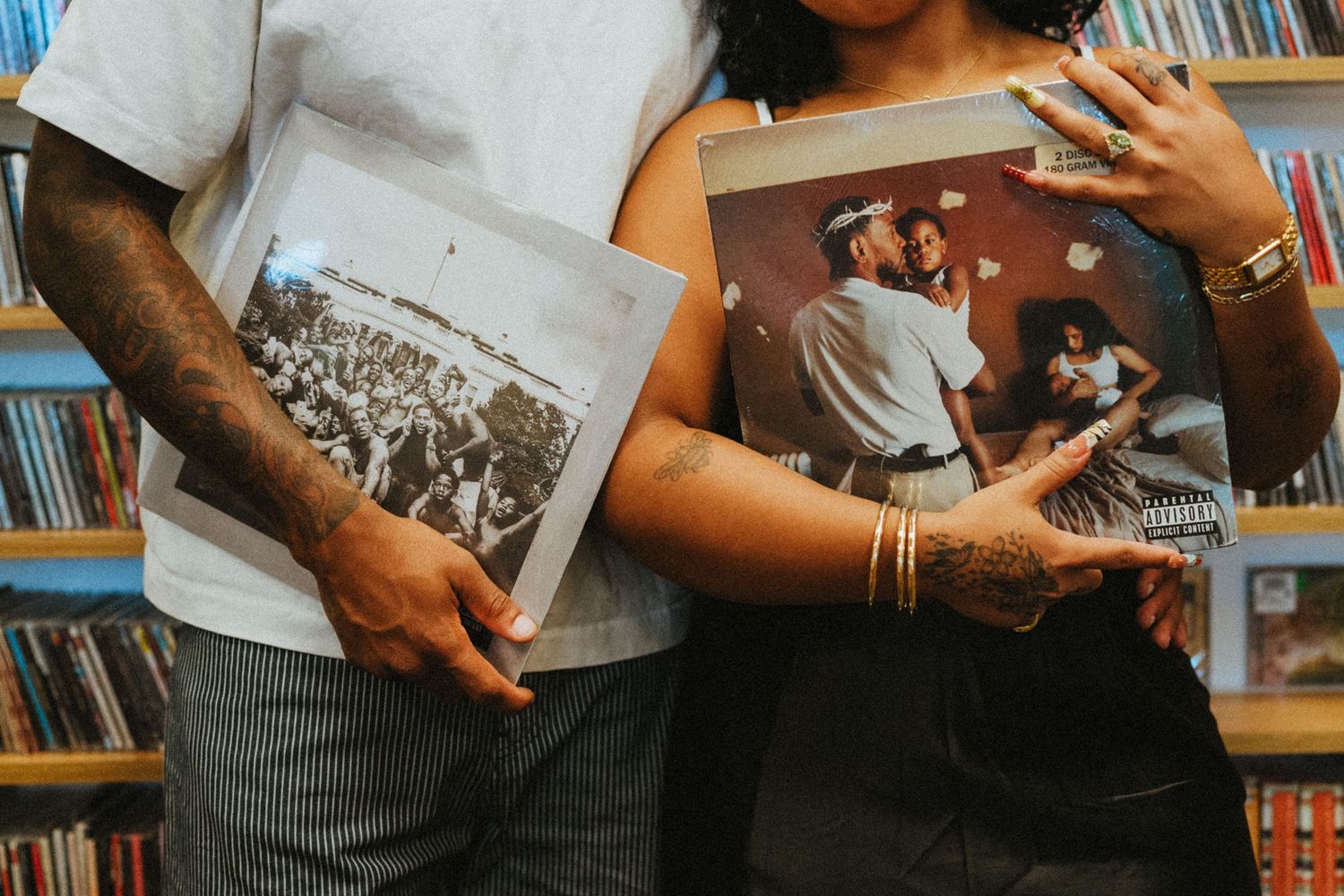 Couple embracing in a record store, each holding vintage vinyl album covers among shelves of records.