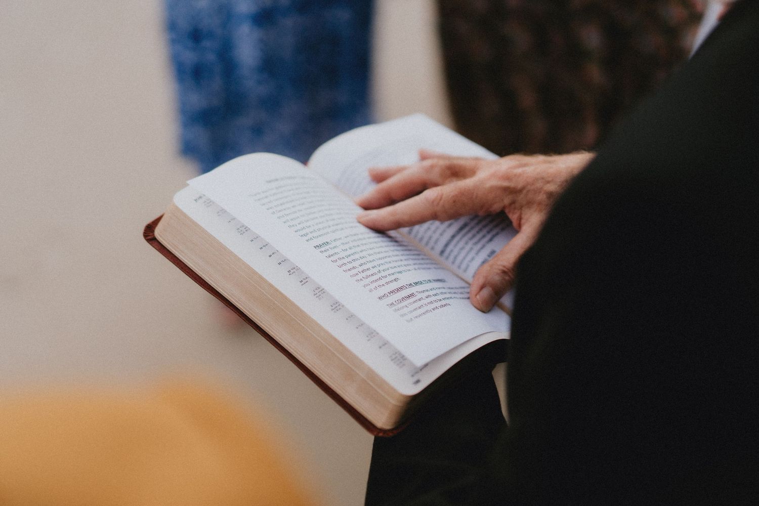 Person reading open Bible with hand resting on pages indoors.