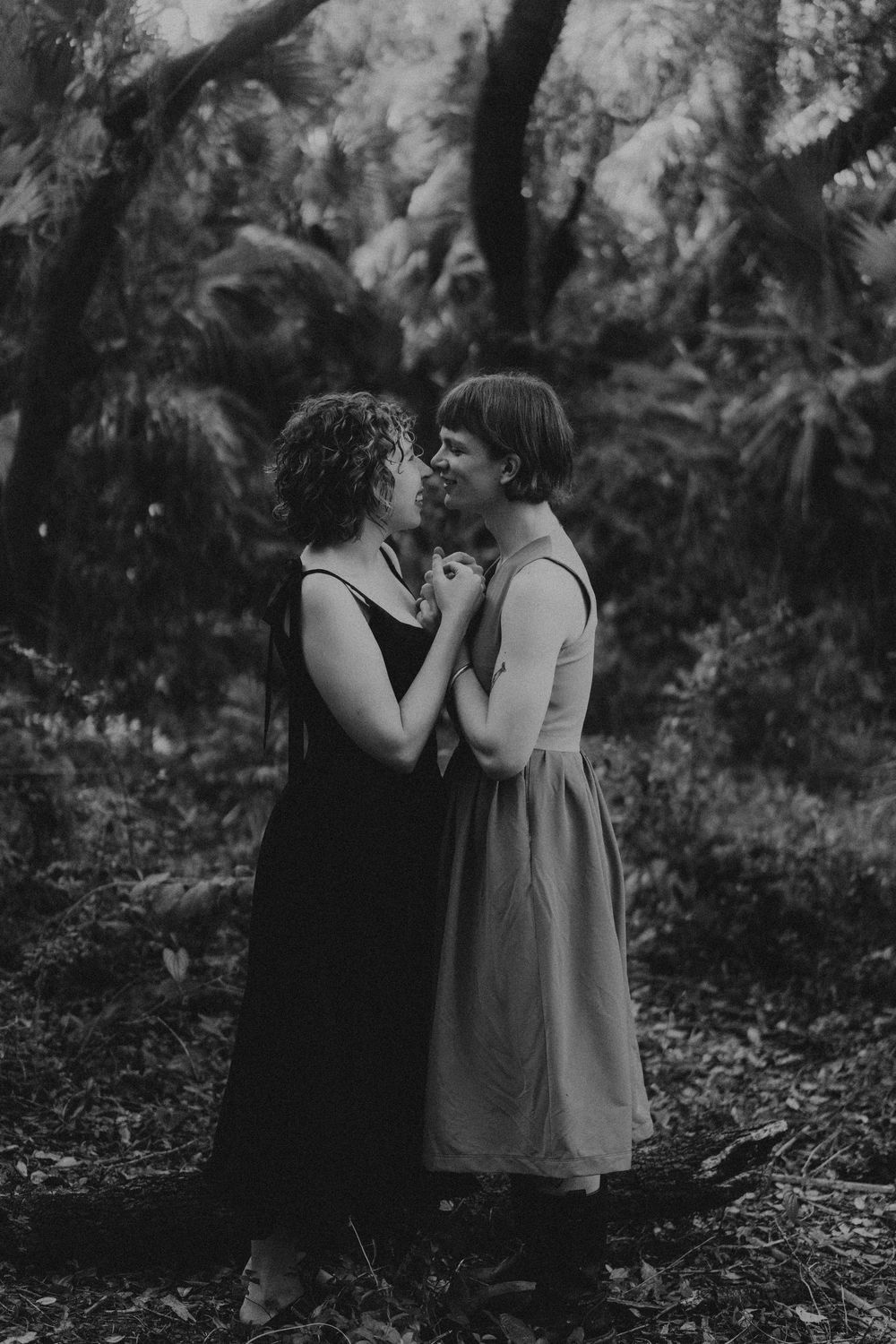 A romantic black and white portrait captured in a wooded outdoor setting.