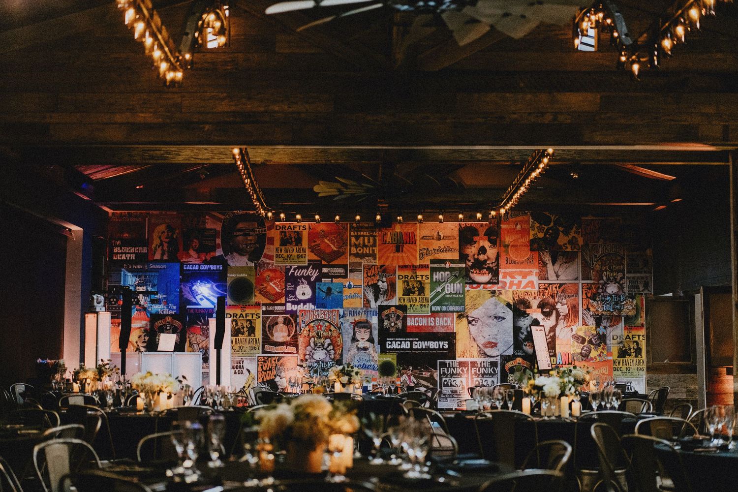 Elegant wedding reception venue with colorful vintage posters on walls, string lights, and formally set dining tables.