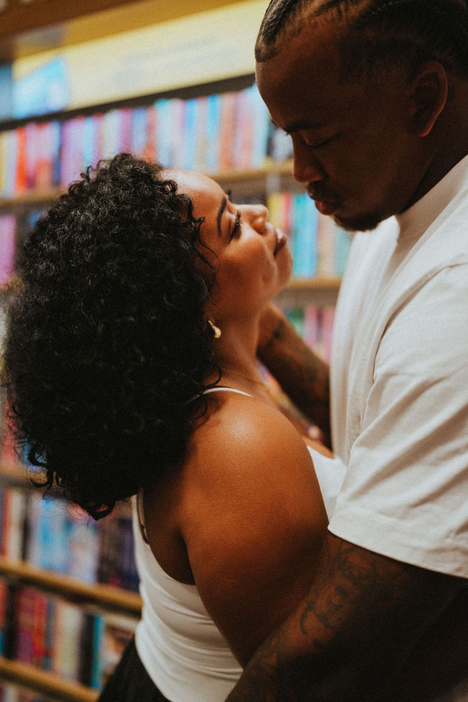 A couple shares an intimate moment in a colorful bookstore, gazing lovingly at each other.