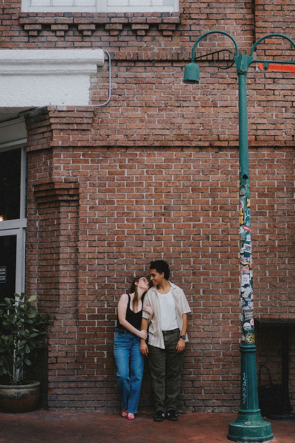 A romantic moment shared against a brick wall backdrop with green lamp posts.