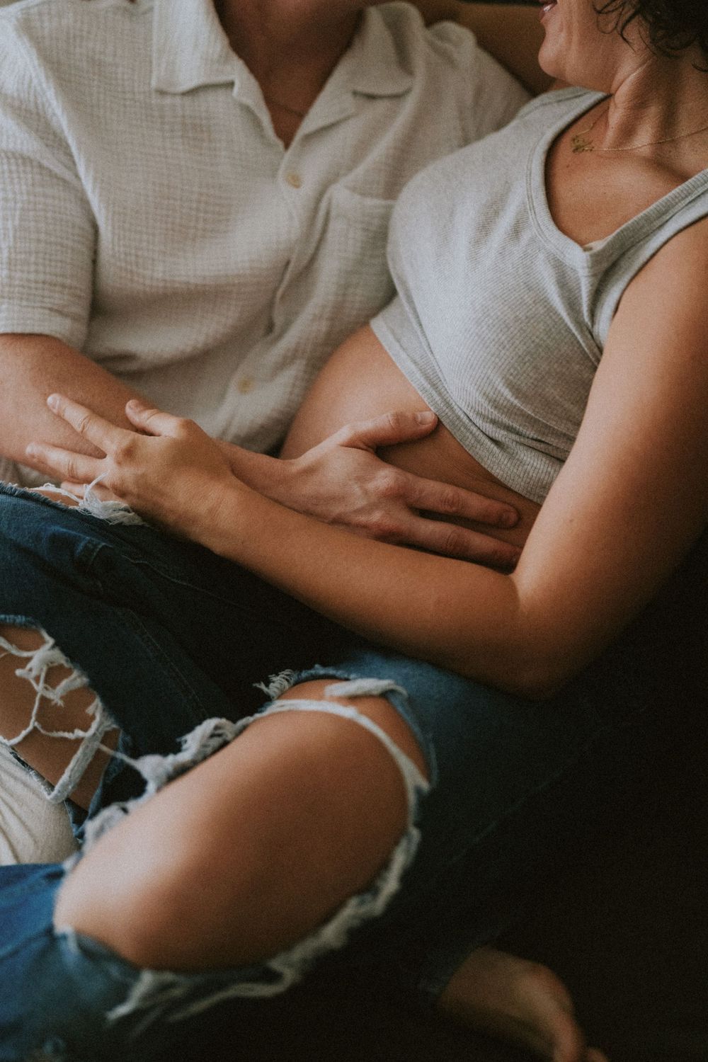 Close-up shot of people sitting together on couch wearing casual clothing with distressed denim jeans.