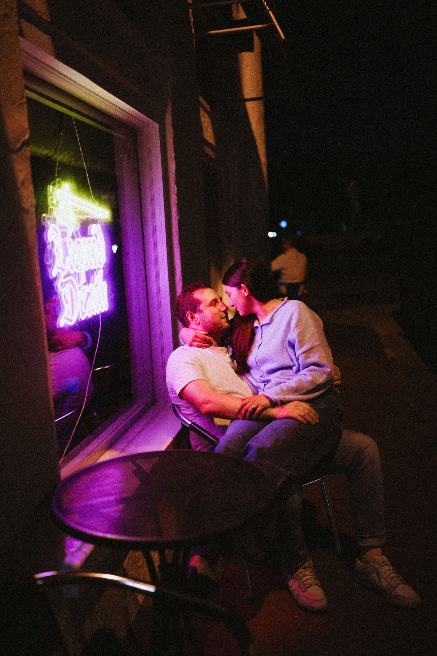 Couple sharing a romantic moment outside a neon-lit diner at night, bathed in purple and green light.