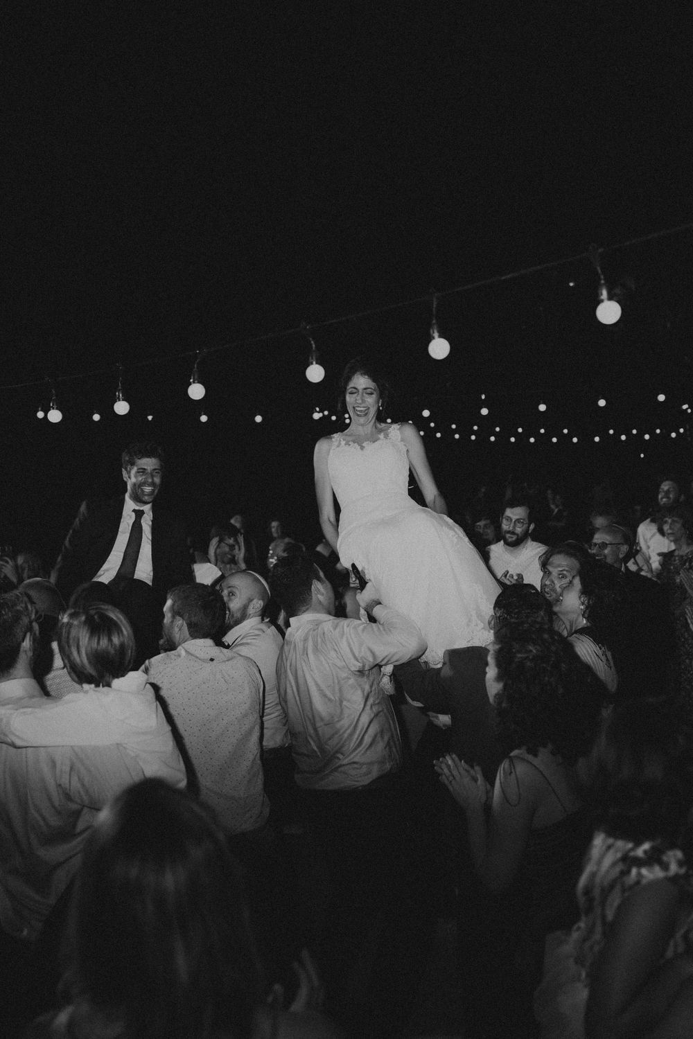Wedding guests dancing under string lights at an outdoor evening reception.