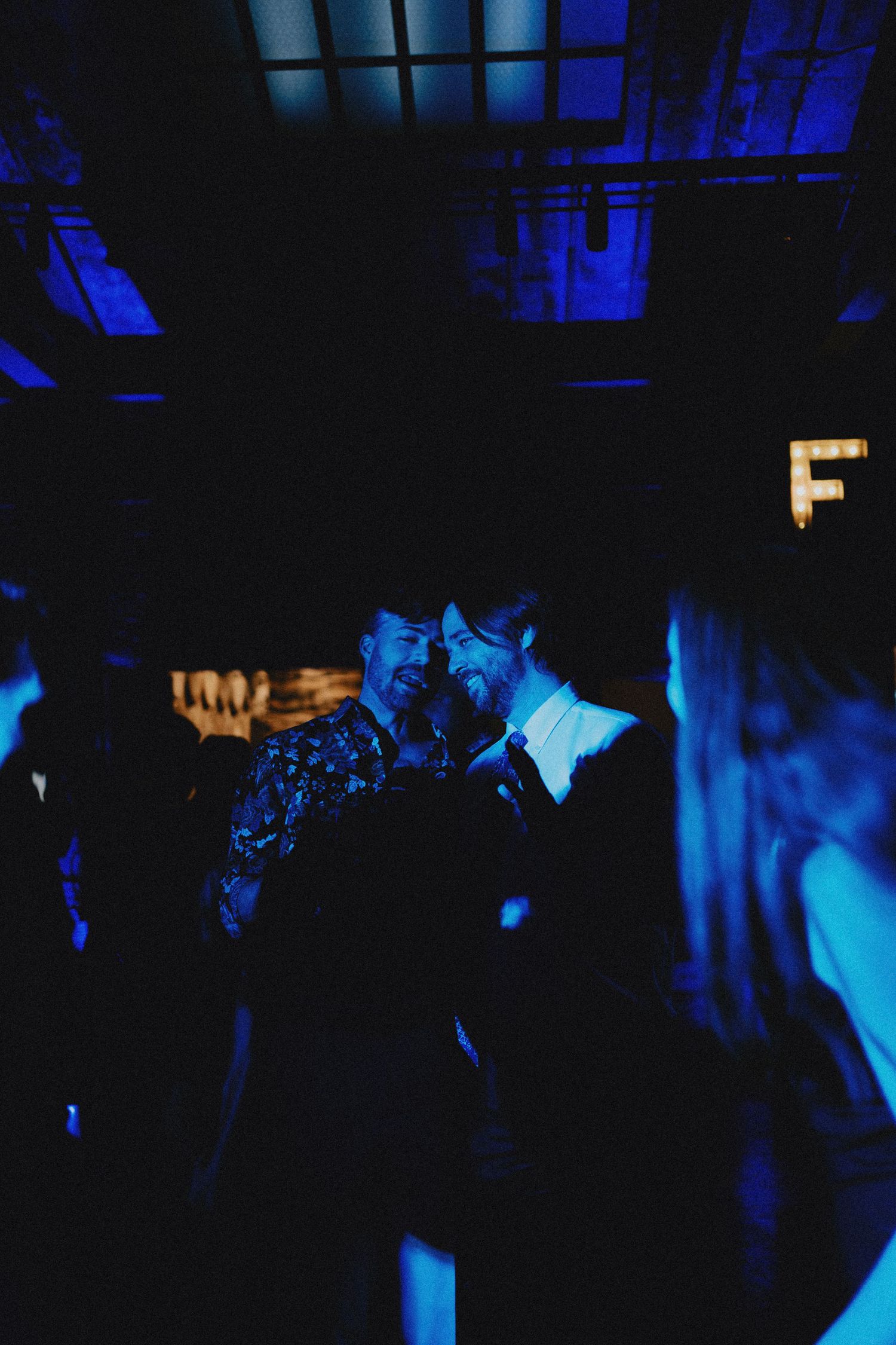 Two people share an intimate moment on a dark dance floor bathed in blue light.
