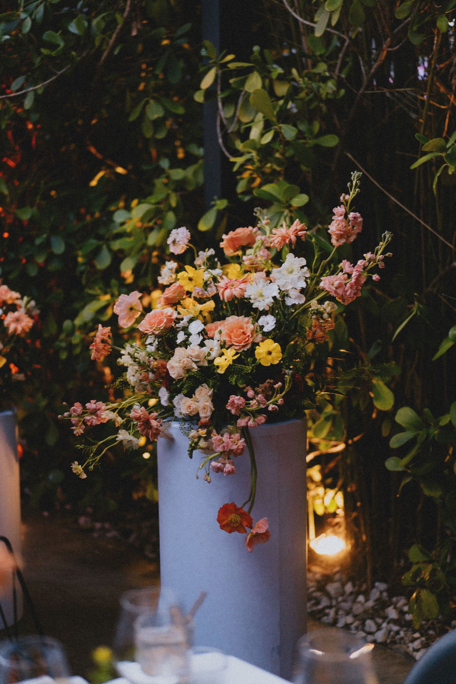 Elegant wedding floral arrangement of pink, yellow, and white blooms in a gray vase amid garden greenery.