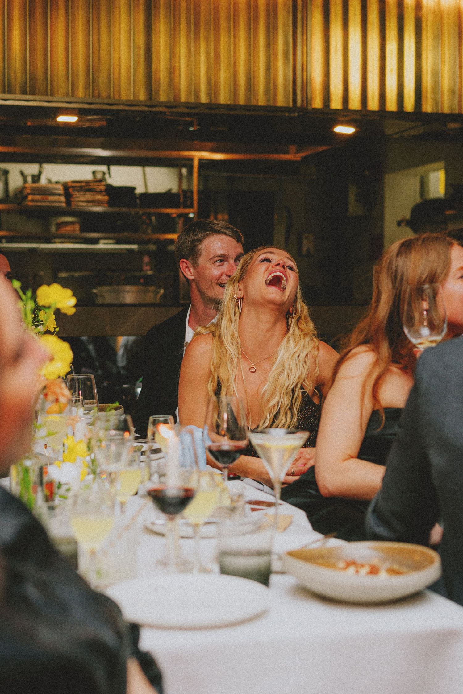 Bride laughing joyfully with guests at elegant wedding reception dinner table.