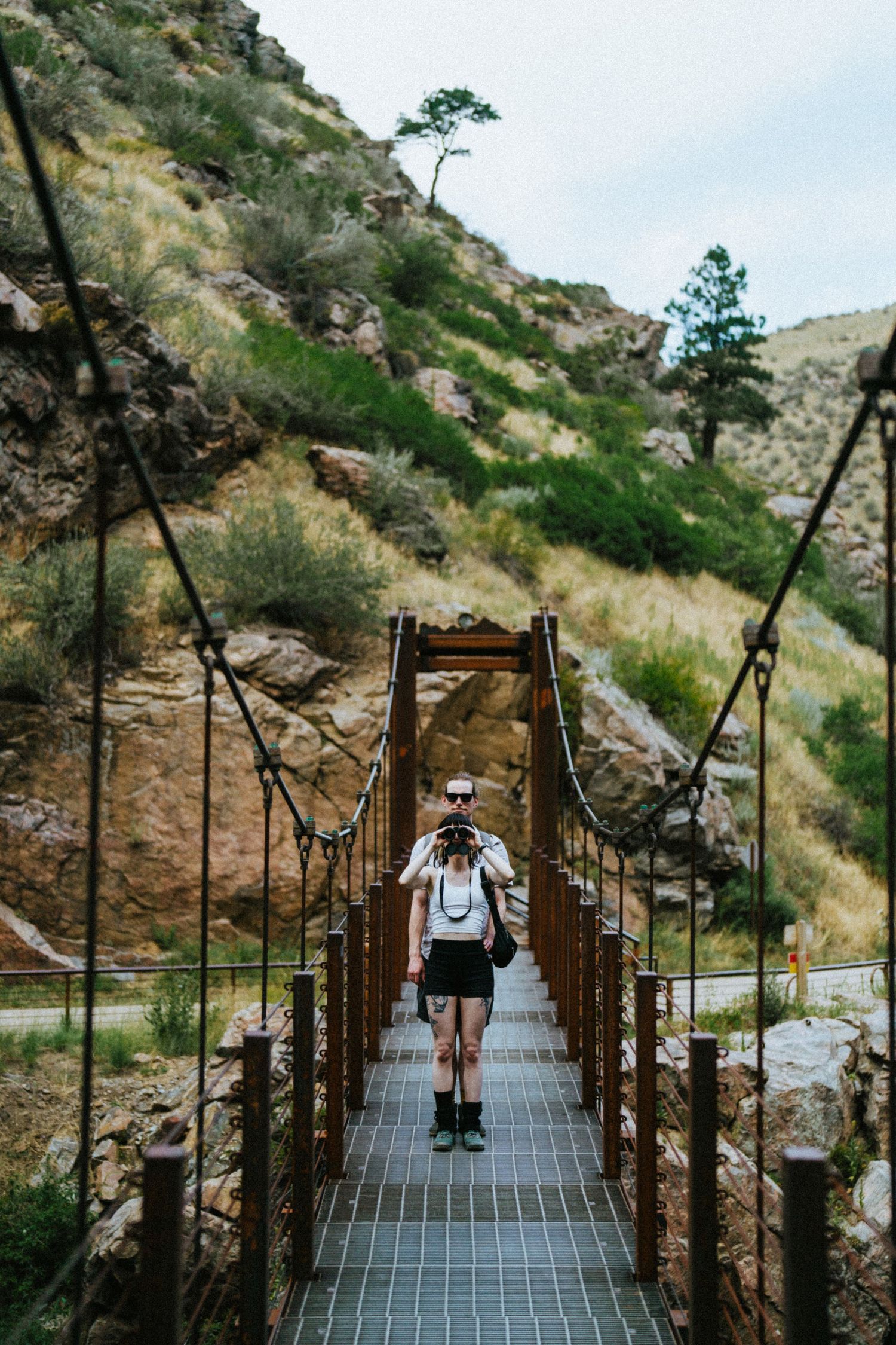 Hiker with backpack crossing a wooden suspension bridge in a rocky mountain canyon with green trees.