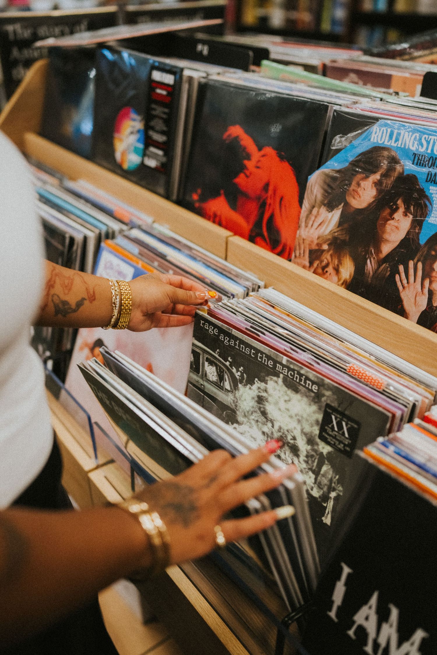 Tattooed hands browsing vinyl records at a music store, including Rage Against the Machine album.