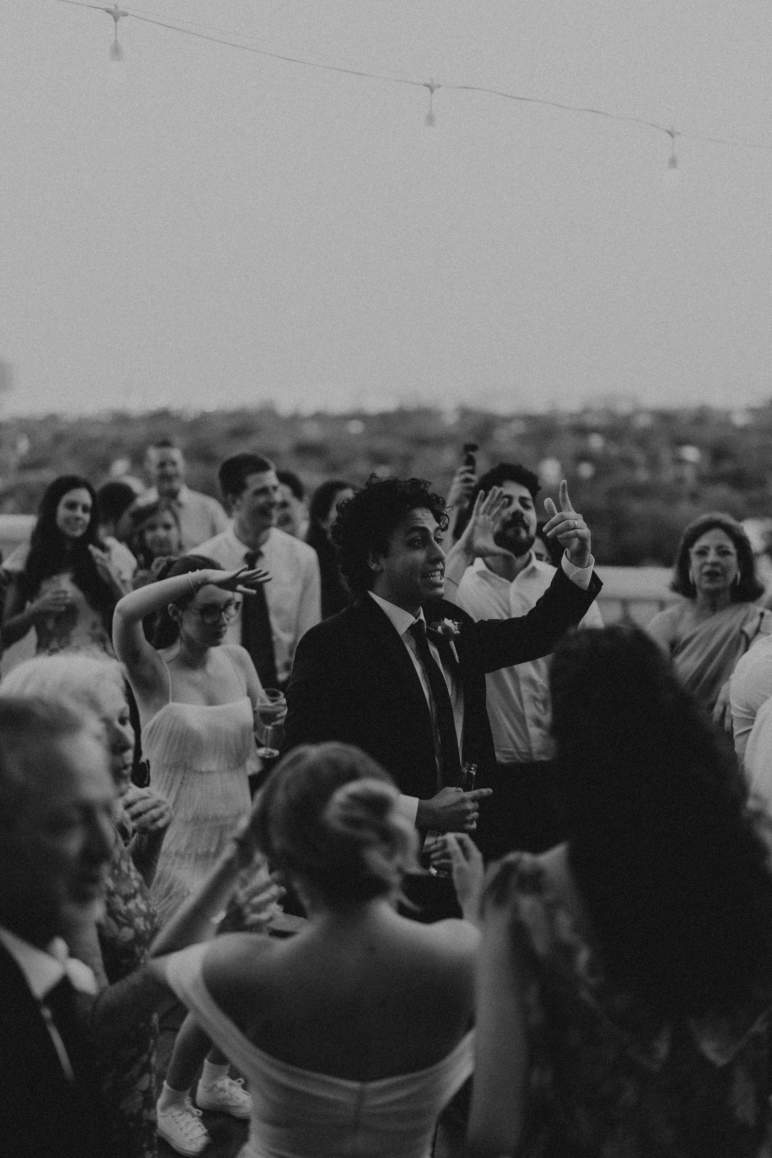Black and white photo of wedding guests dancing and celebrating at an outdoor reception.