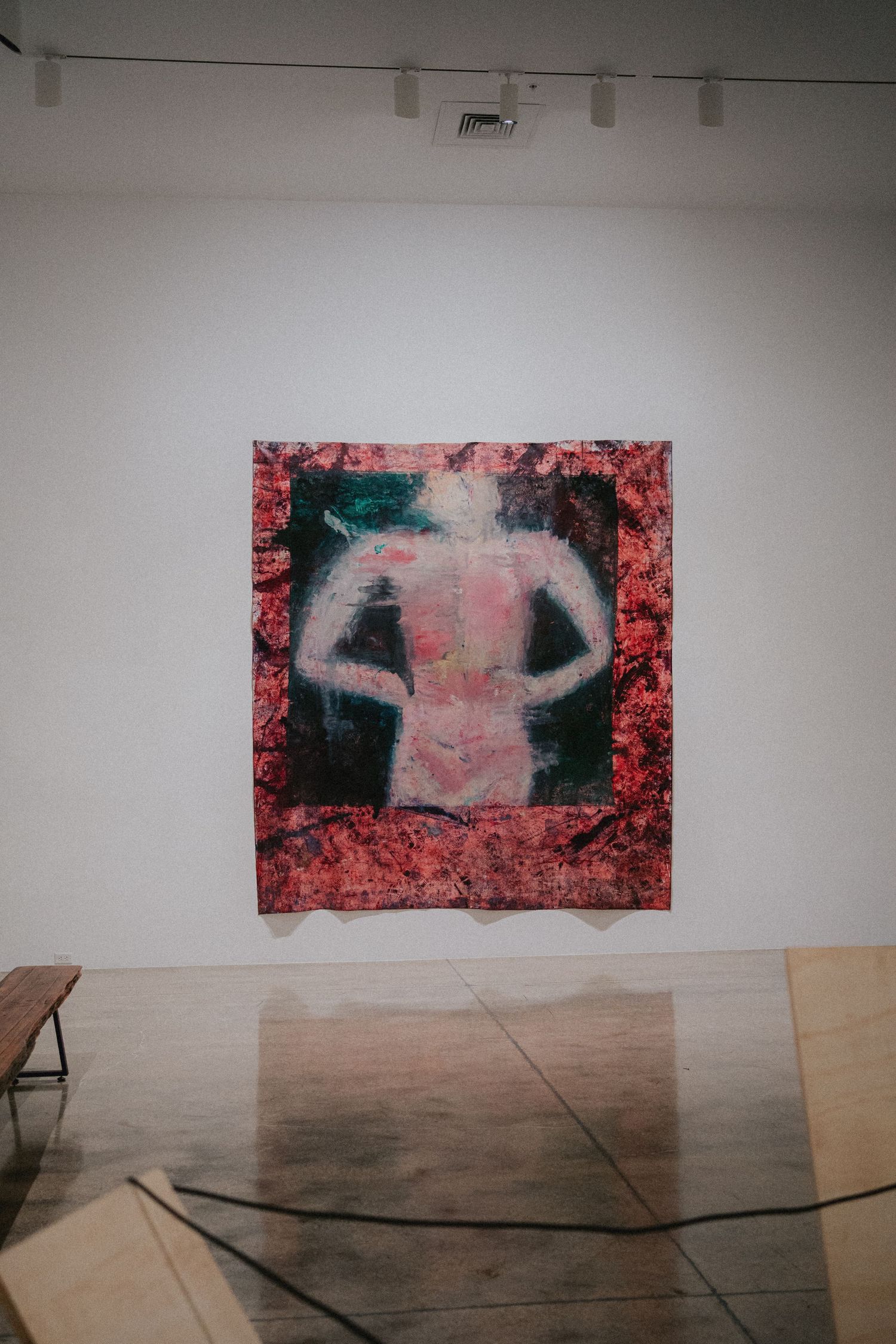 Abstract figurative painting of a human back displayed on a white gallery wall, surrounded by red floral imagery.