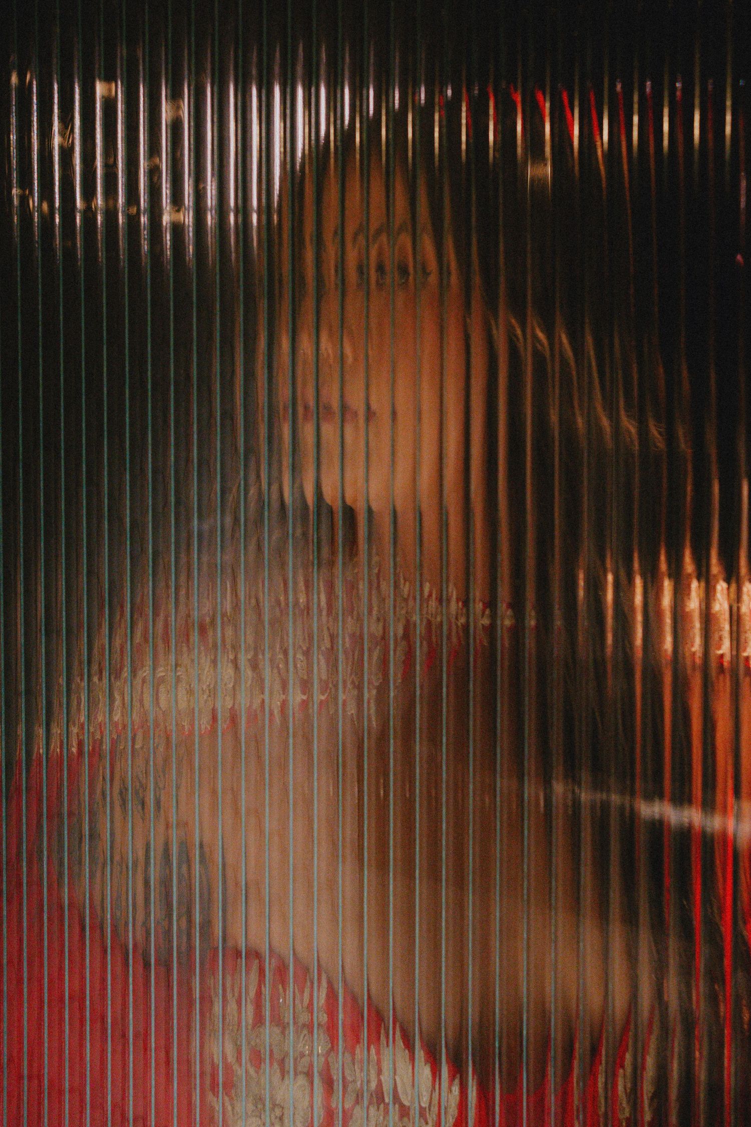 A blurred silhouette of a person viewed through ribbed glass with warm red and orange tones.