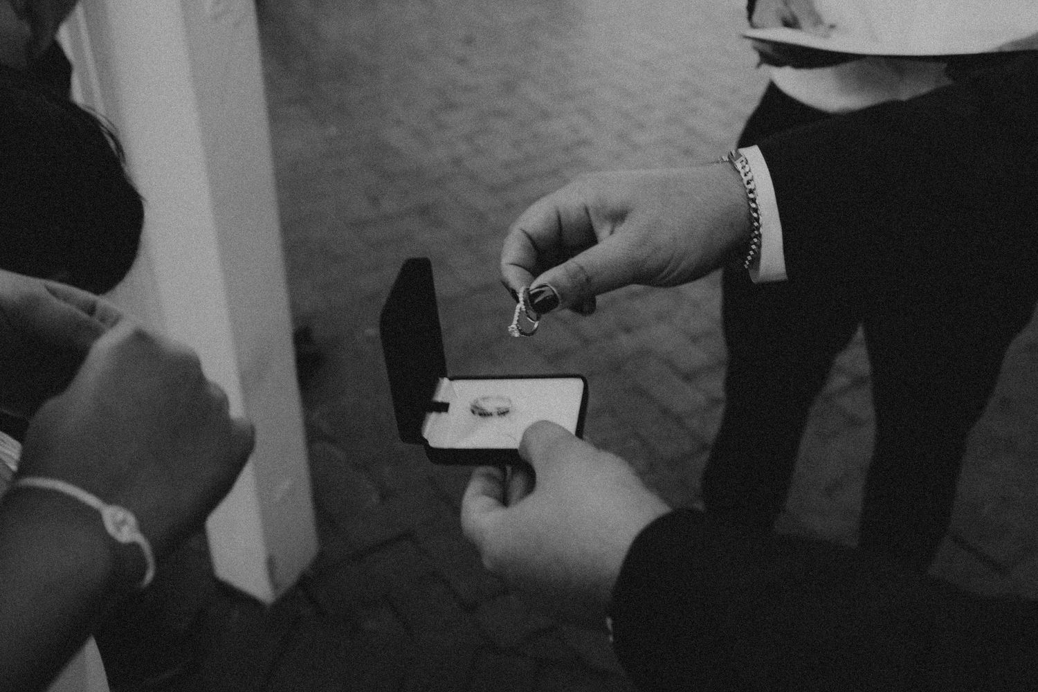 Black and white photo of hands exchanging a ring in a box at a wedding ceremony.