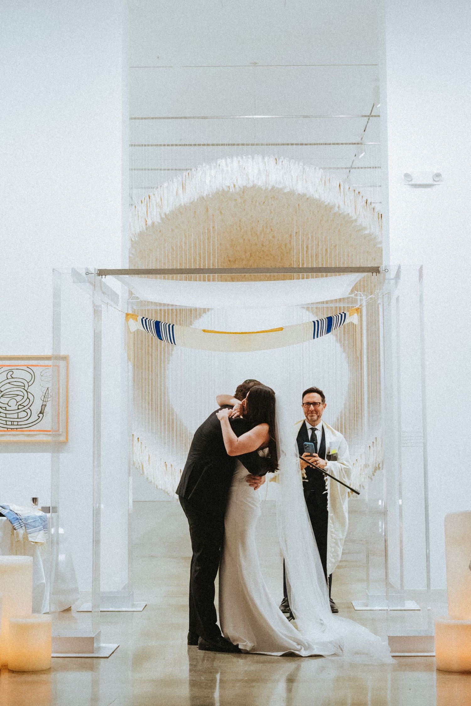 Couple shares first kiss under elegant chuppah at modern art gallery wedding ceremony.