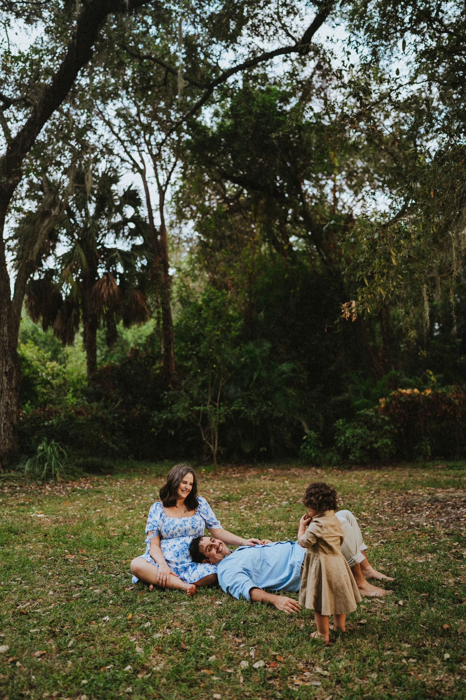 A couple and their golden retriever dog relax together on autumn leaves in a park setting.