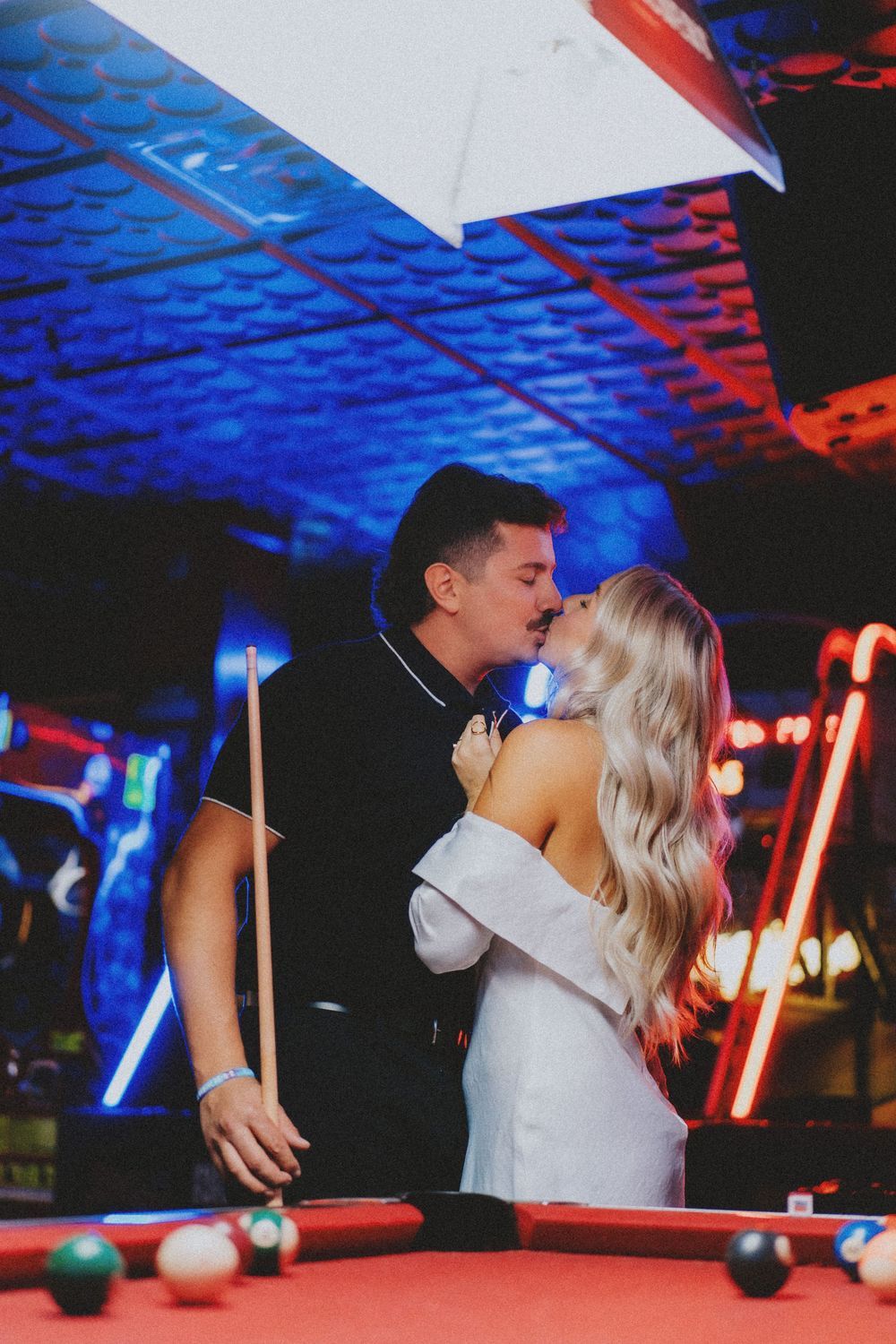Romantic couple sharing intimate moments around a pool table with blue lighting.