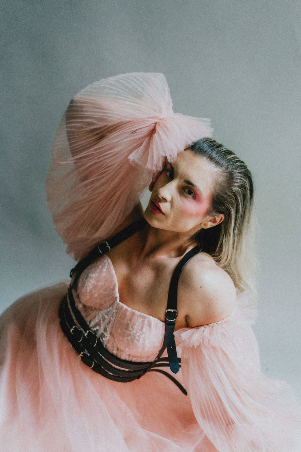 Fashion portrait featuring pink tulle fabric and black harness against grey backdrop.