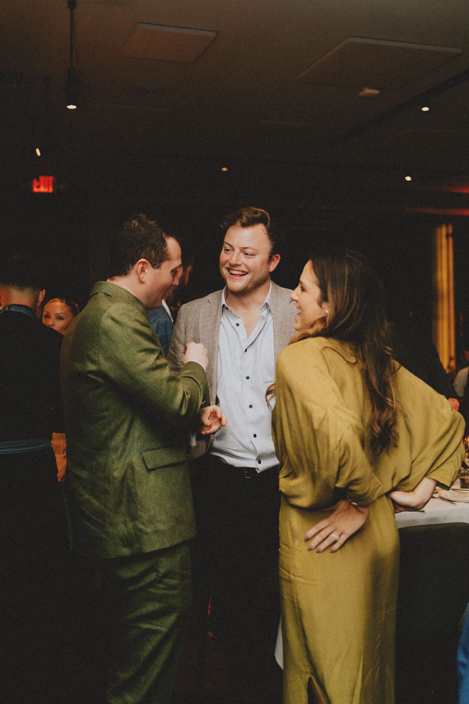 Three wedding guests laughing and socializing at a dimly lit wedding reception venue.