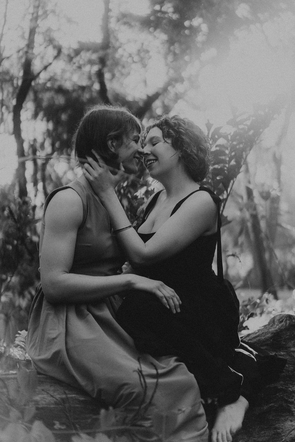 Two people share an intimate moment in a dreamy black and white forest setting.