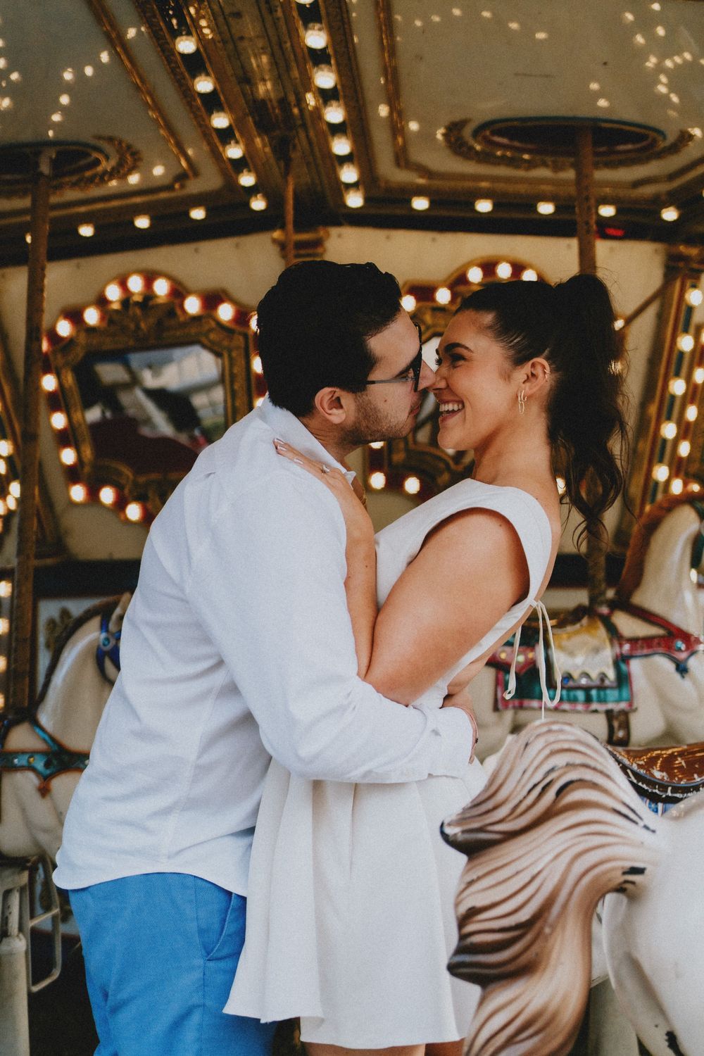 A tender moment captured on a carousel with twinkling lights in the background.