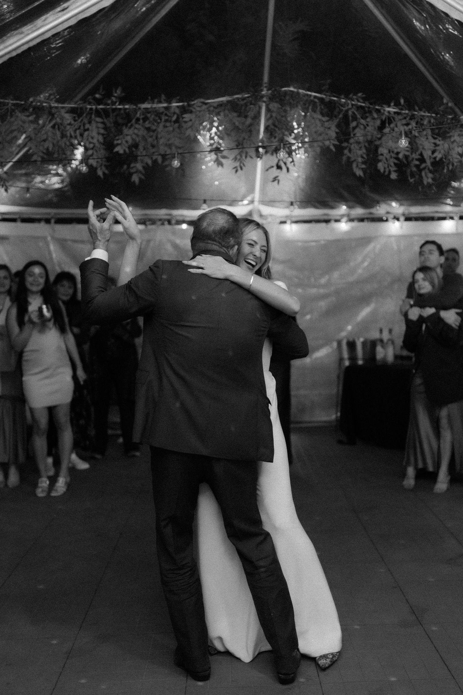 Black and white photo of bride and groom sharing first dance under tented reception venue.