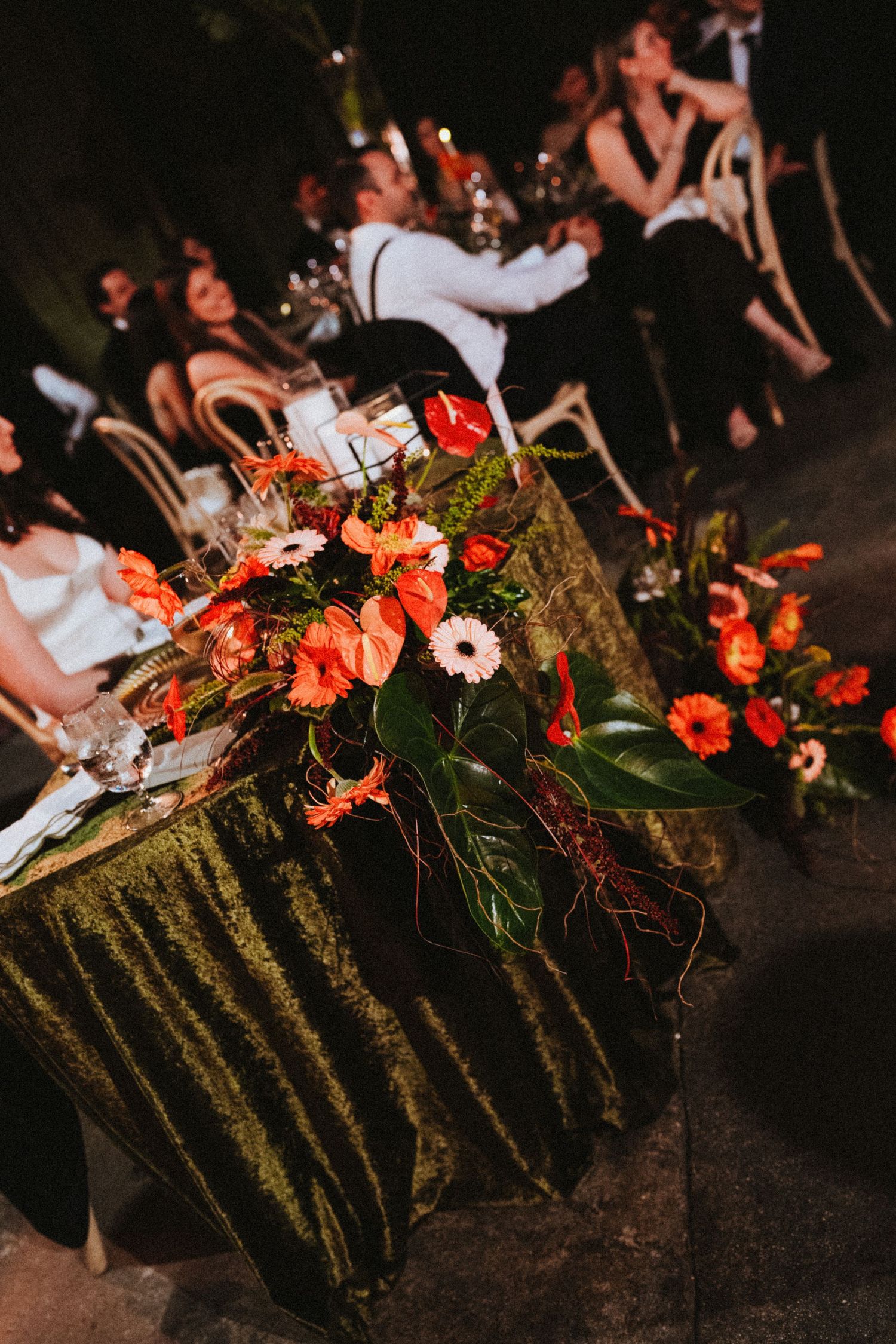 Elegant wedding reception table with lush orange and red floral arrangements on a moss-green velvet tablecloth.