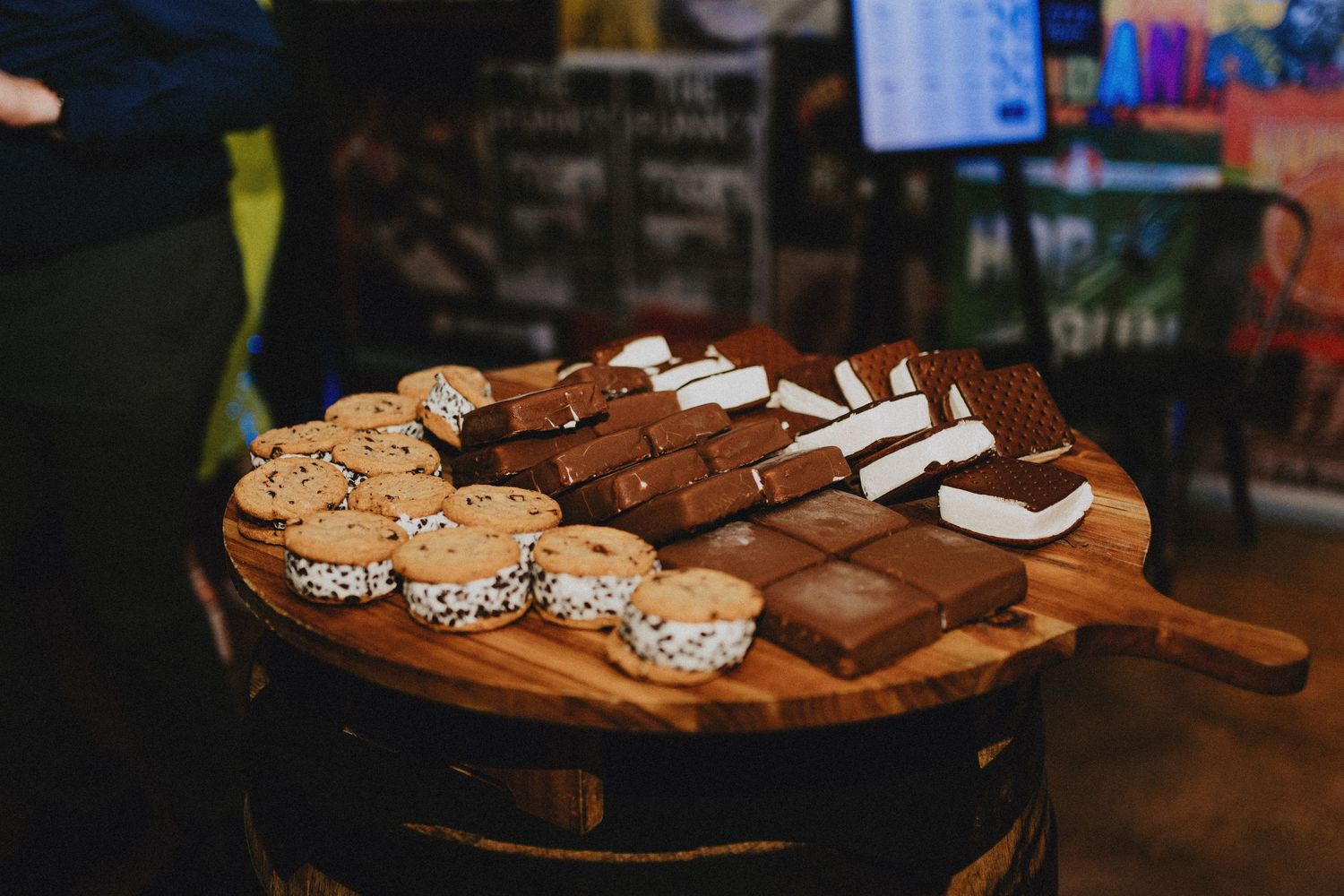 Assorted desserts on a wooden board, featuring chocolate s'mores bars and rice crispy treats at a party.