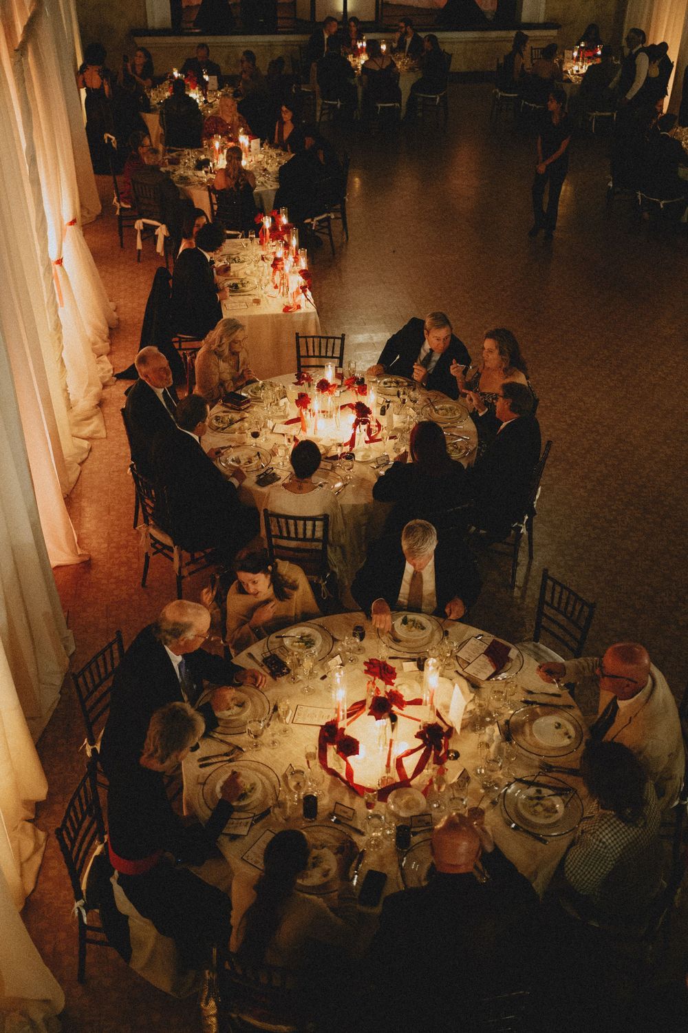 Overhead view of wedding reception with round tables and red centerpieces in dimly lit ballroom.