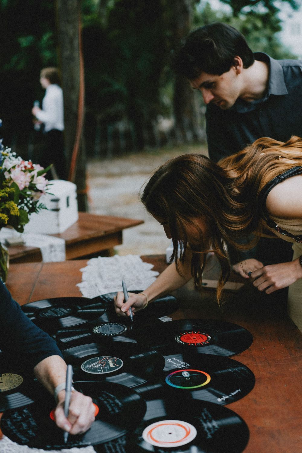 People signing vinyl records laid out on a dark wooden surface at an event.
