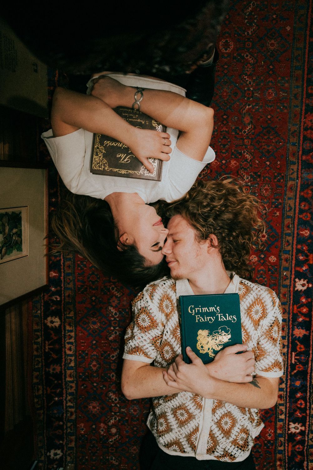 A couple lying on a patterned rug holding a Grimm fairy tales book during an intimate photoshoot.