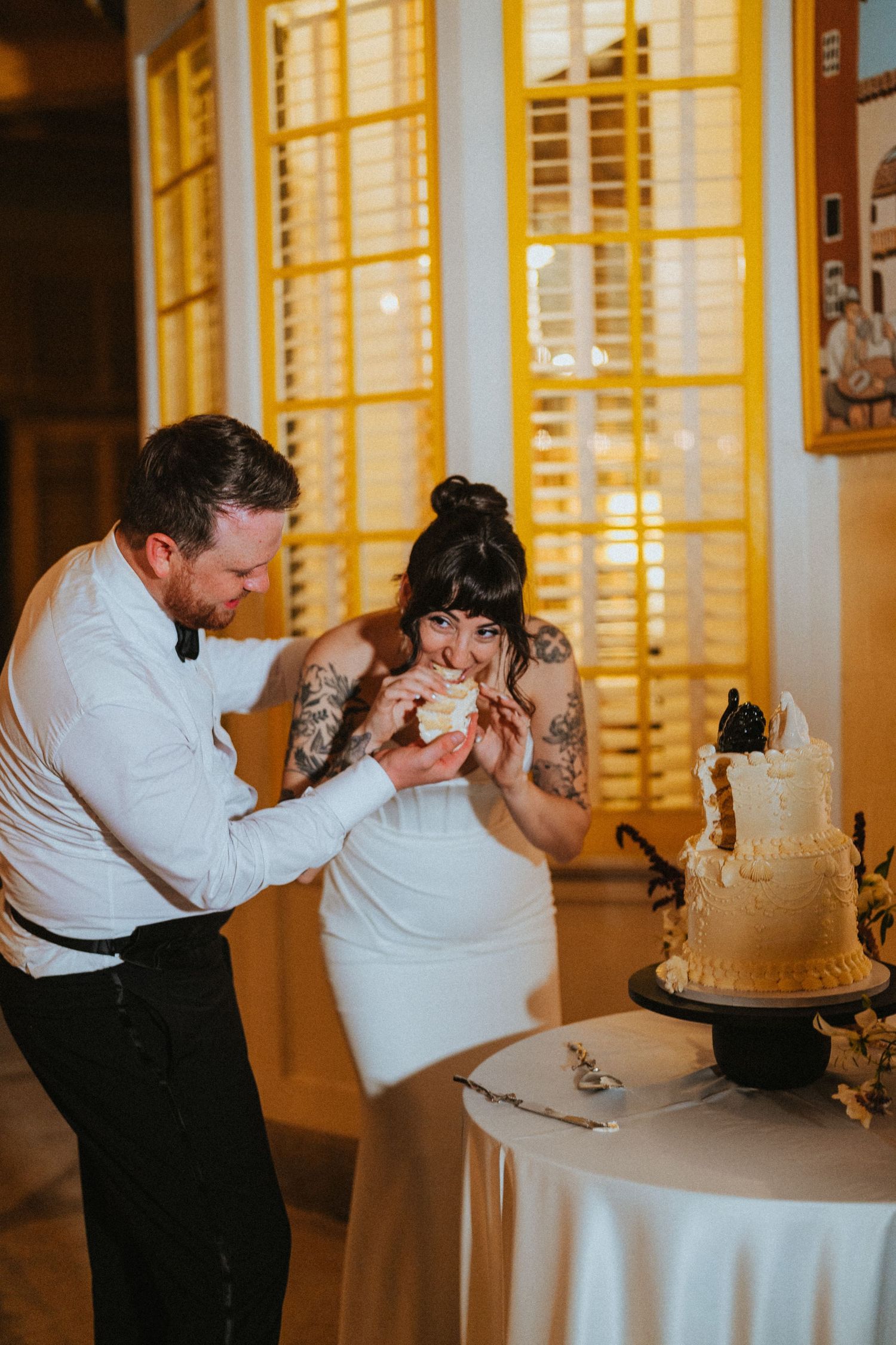Groom feeds bride a slice of wedding cake during fun cake cutting ceremony at reception.