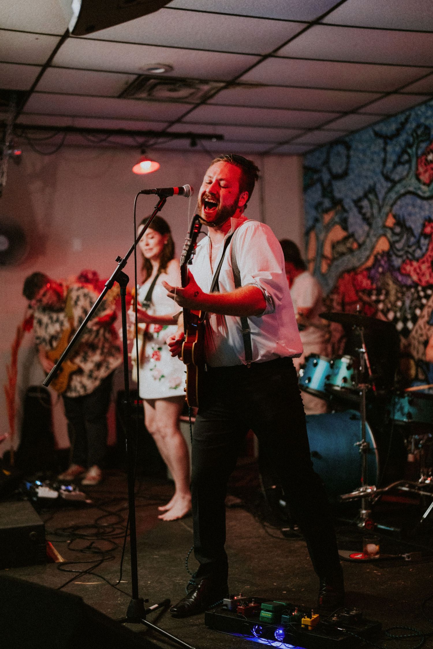 A passionate guitarist and vocalist performs on stage at a wedding reception with a colorful mural backdrop.