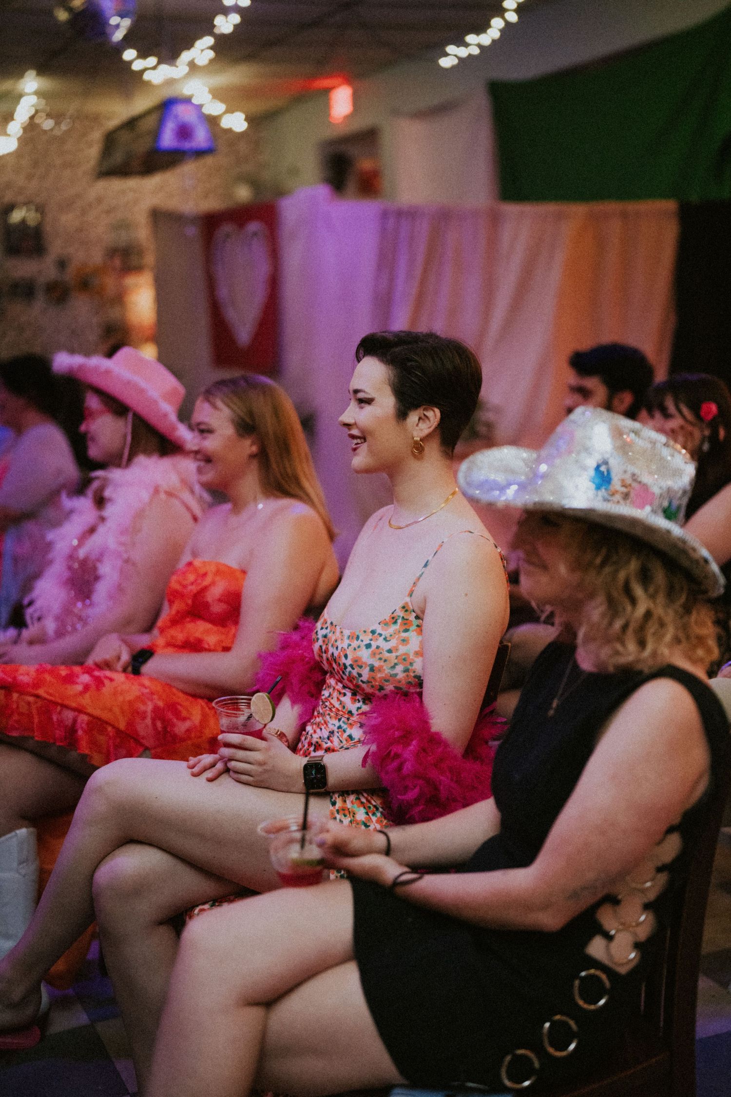 Wedding guests in colorful dresses and cowboy hats laugh and celebrate at a festive indoor reception.