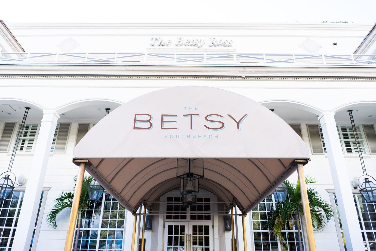Exterior view of The Betsy Hotel entrance with elegant awning and white colonial architecture in Miami Beach.